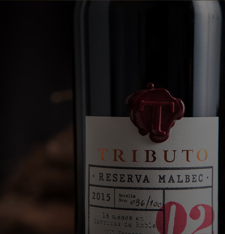 Close-up of a wine bottle labeled "Tributo Reserva Malbec" with vintage 2015. A red wax seal with a "T" adorns the refined packaging, conveying elegance.