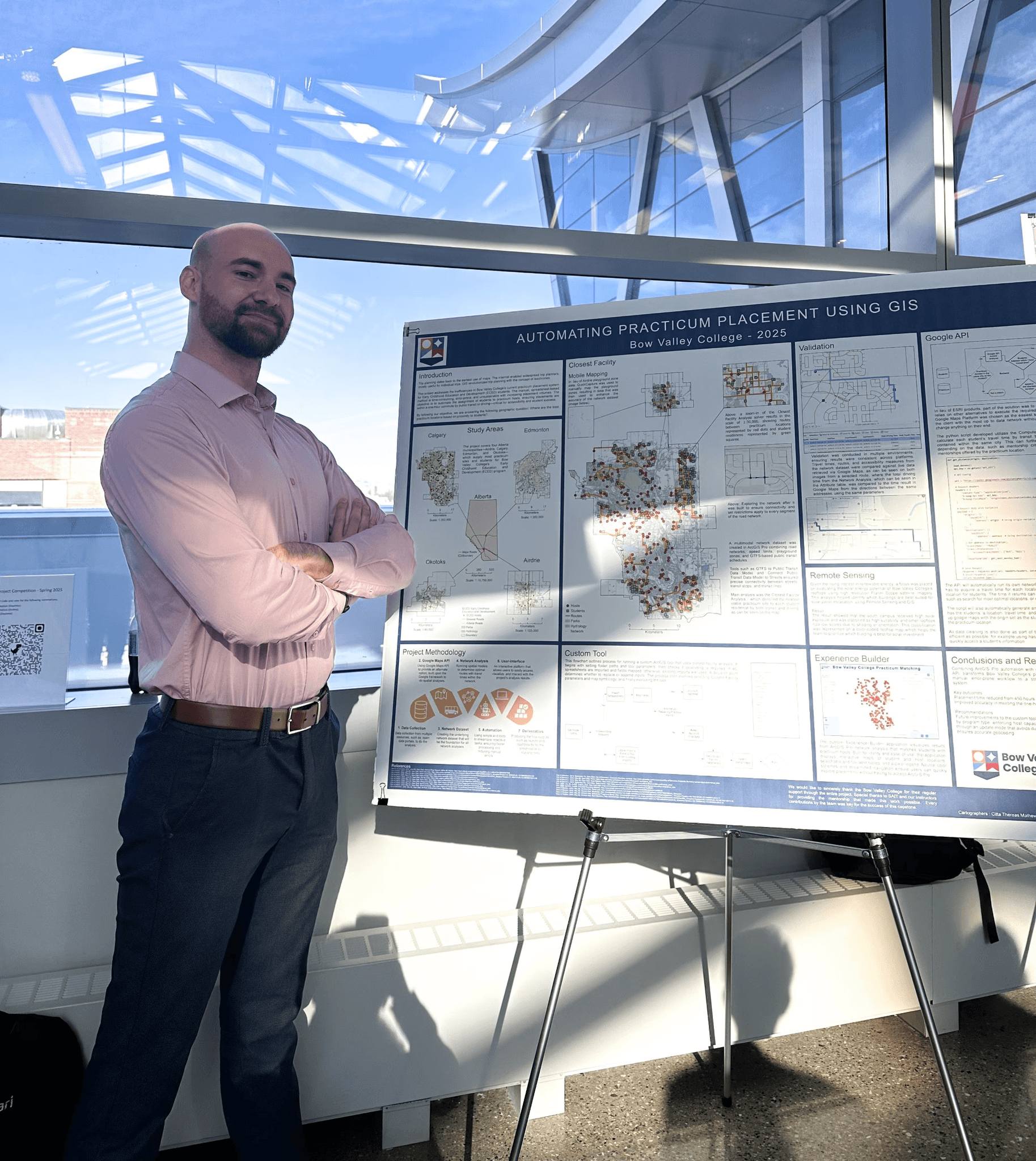 A young person with curly hair smiles at the camera while sitting in front of a laptop against a dark background.
