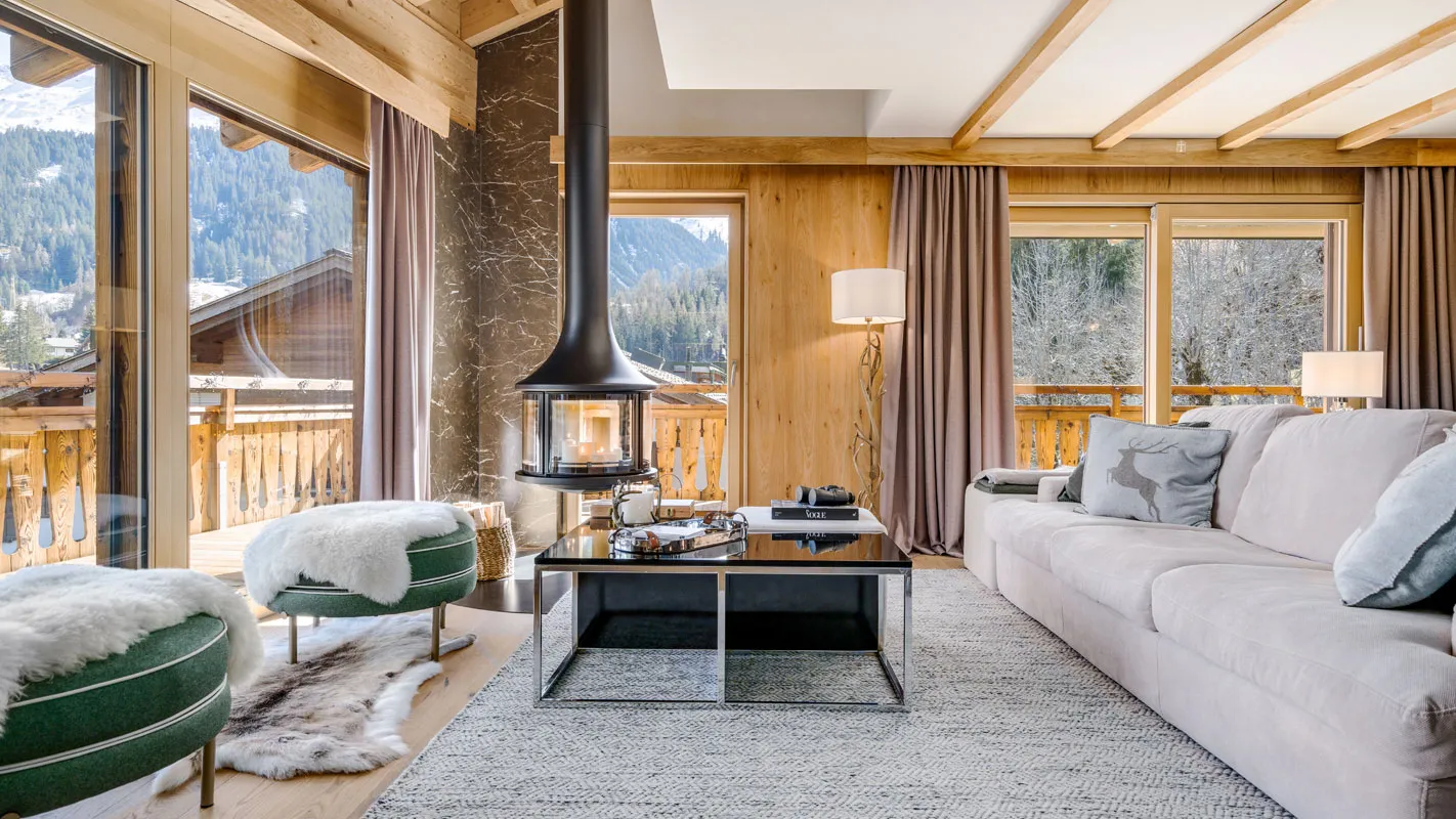 Silvretta Klosters alpine living room with suspended fireplace, timber walls, and panoramic mountain-view windows