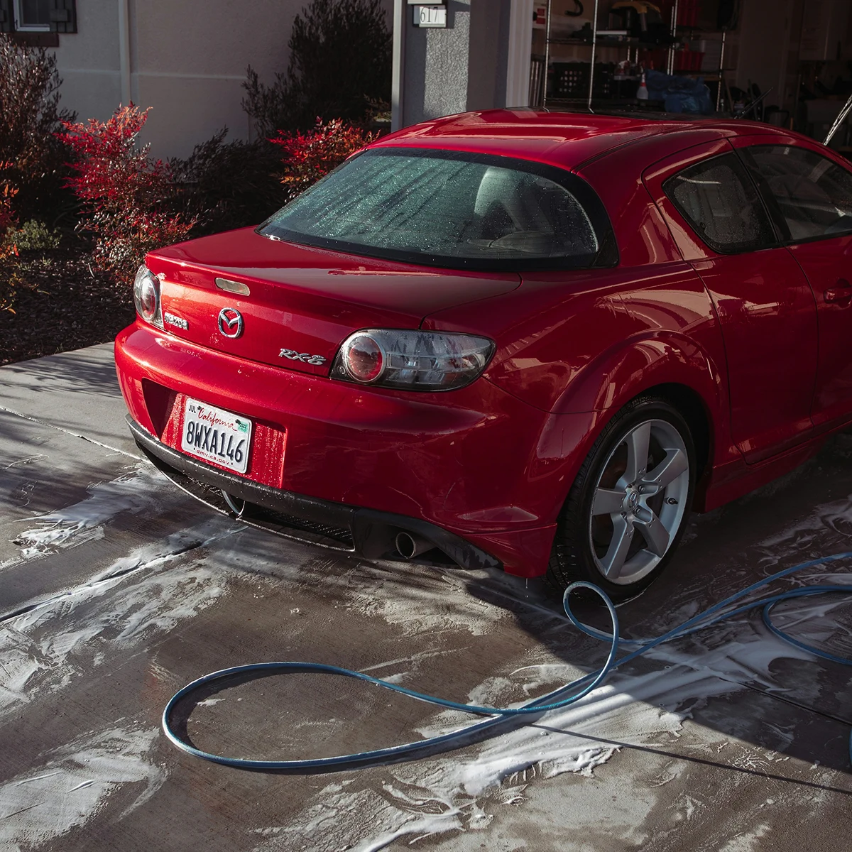 Red Mazda parked in a wash bay with water and cleaning equipment nearby