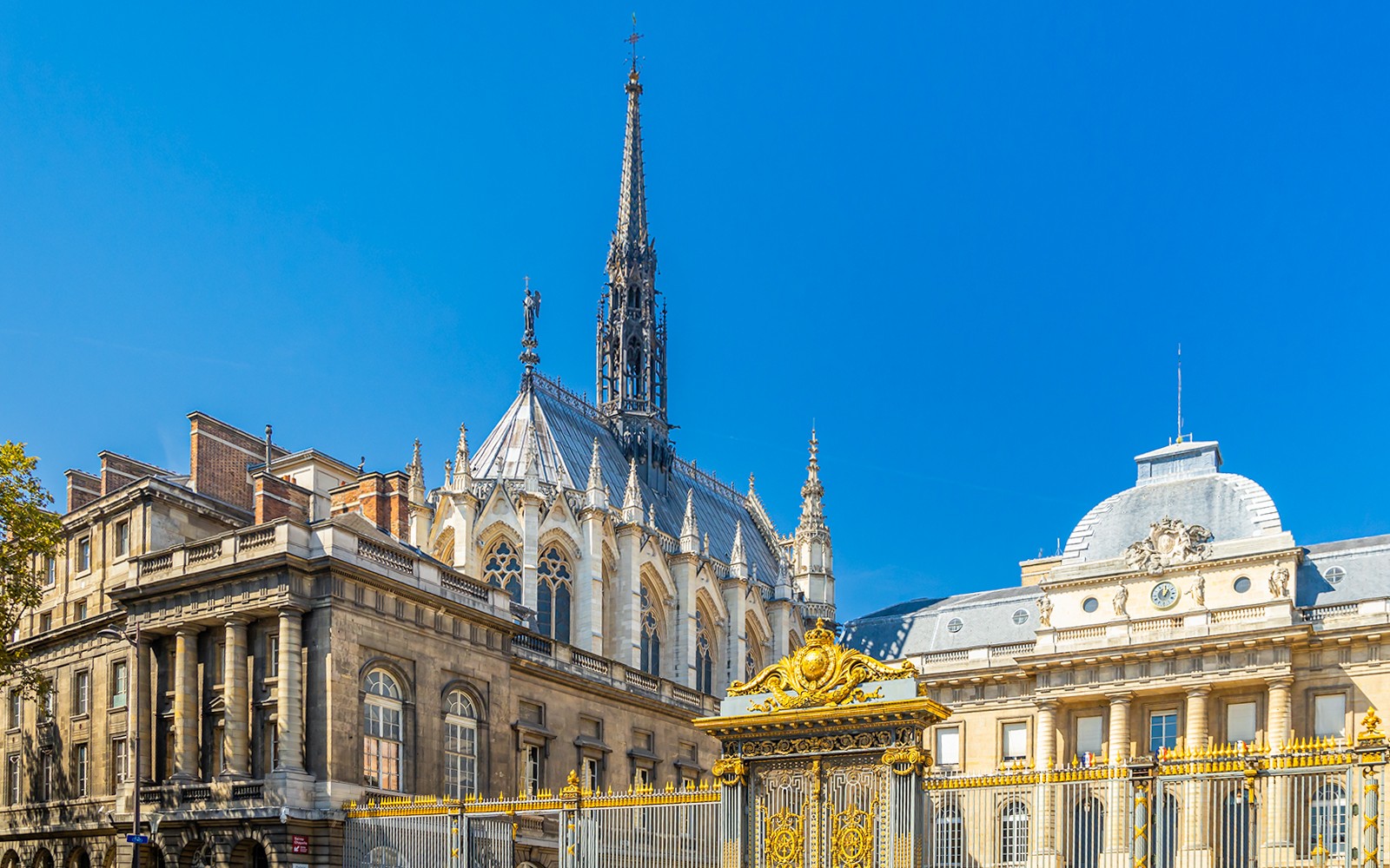 Iglica Sainte Chapelle i fasada Conciergerie w Paryżu z ozdobną złotą bramą.