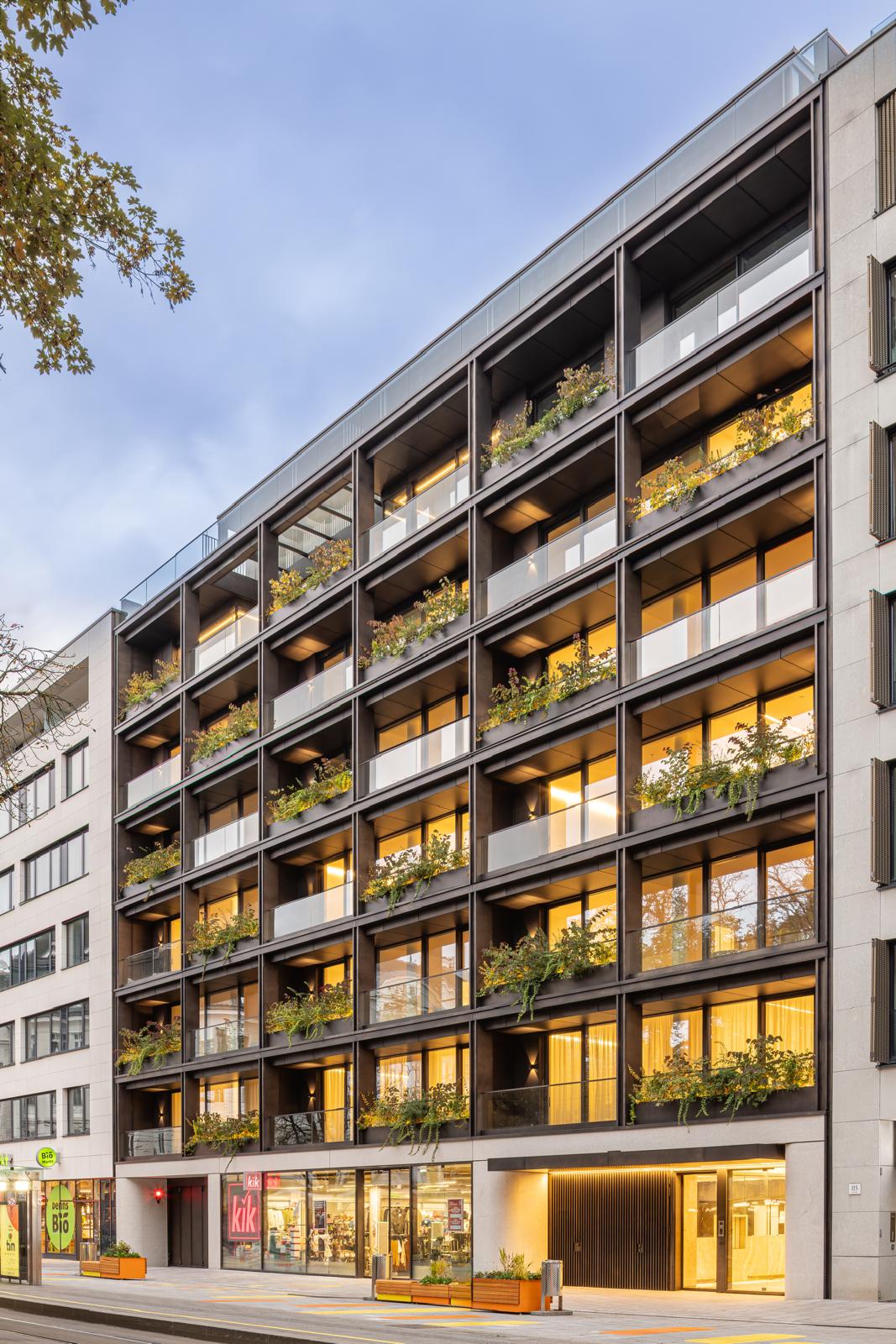 Blick auf die Fassade des Bloom Living Aparthotels in Linz mit modernen Balkonen und großen Fenstern, umgeben von grünen Bäumen