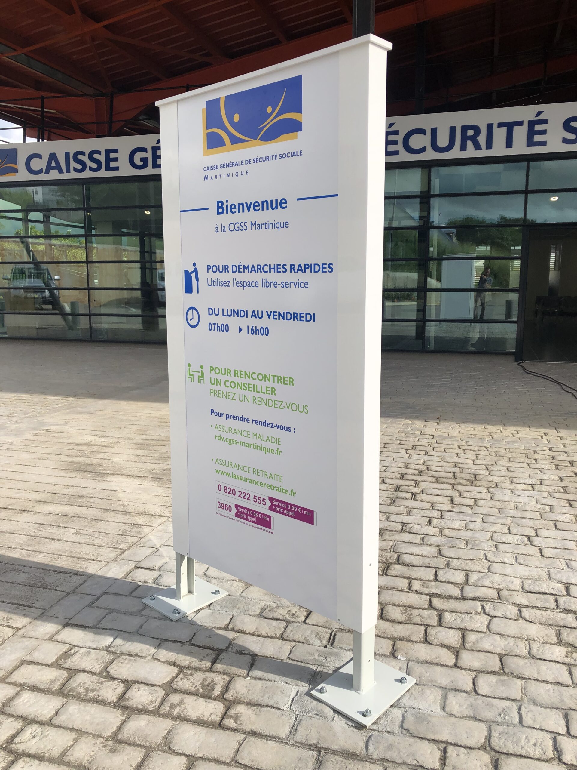 Signalétique extérieure pour CGSS Martinique avec un logo bleu et jaune. Elle fournit des informations sur les procédures rapides et les rendez-vous du lundi au vendredi, de 7 h à 16 h.