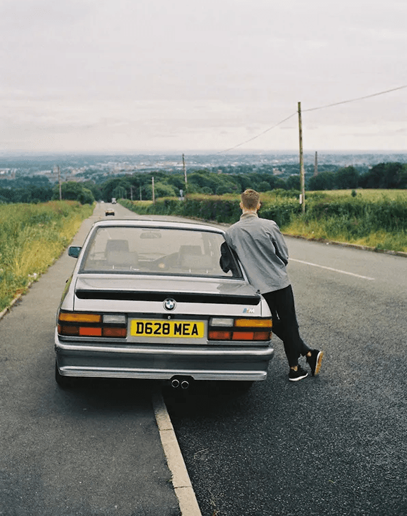 Man leaning on a BMW parked on a rural road