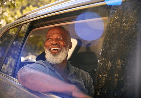 older man in the driver's seat of a parked car, looking thoughtfully out the windscreen
