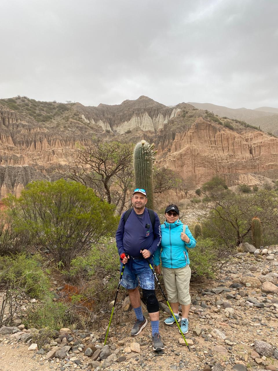 Mujer sentada sobre un tronco frente a una cascada doble en un bosque frondoso de Argentina.