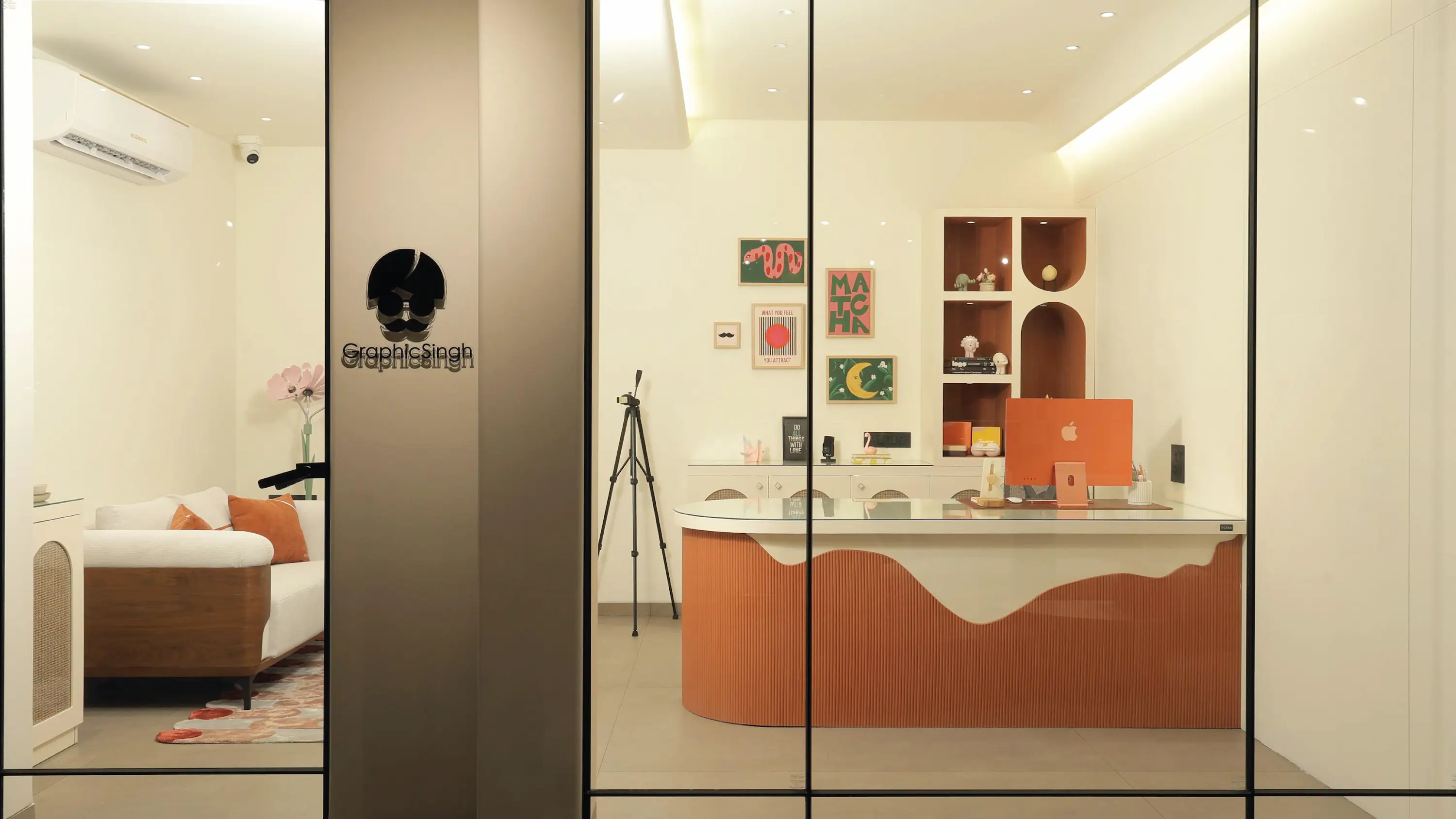 A modern, minimalist office space with glass walls featuring a sleek white desk with a laptop, an artistic wooden partition, and a comfortable seating area, creating a professional and stylish workspace.
