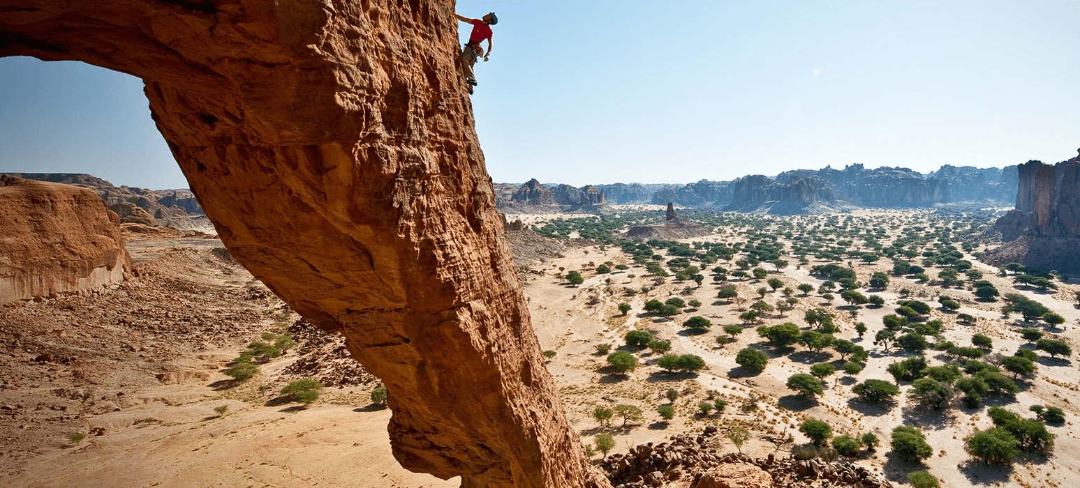 A climber pauses on a rock face to visualize their route on a unique rock formation in the country of Chad in northern Africa.