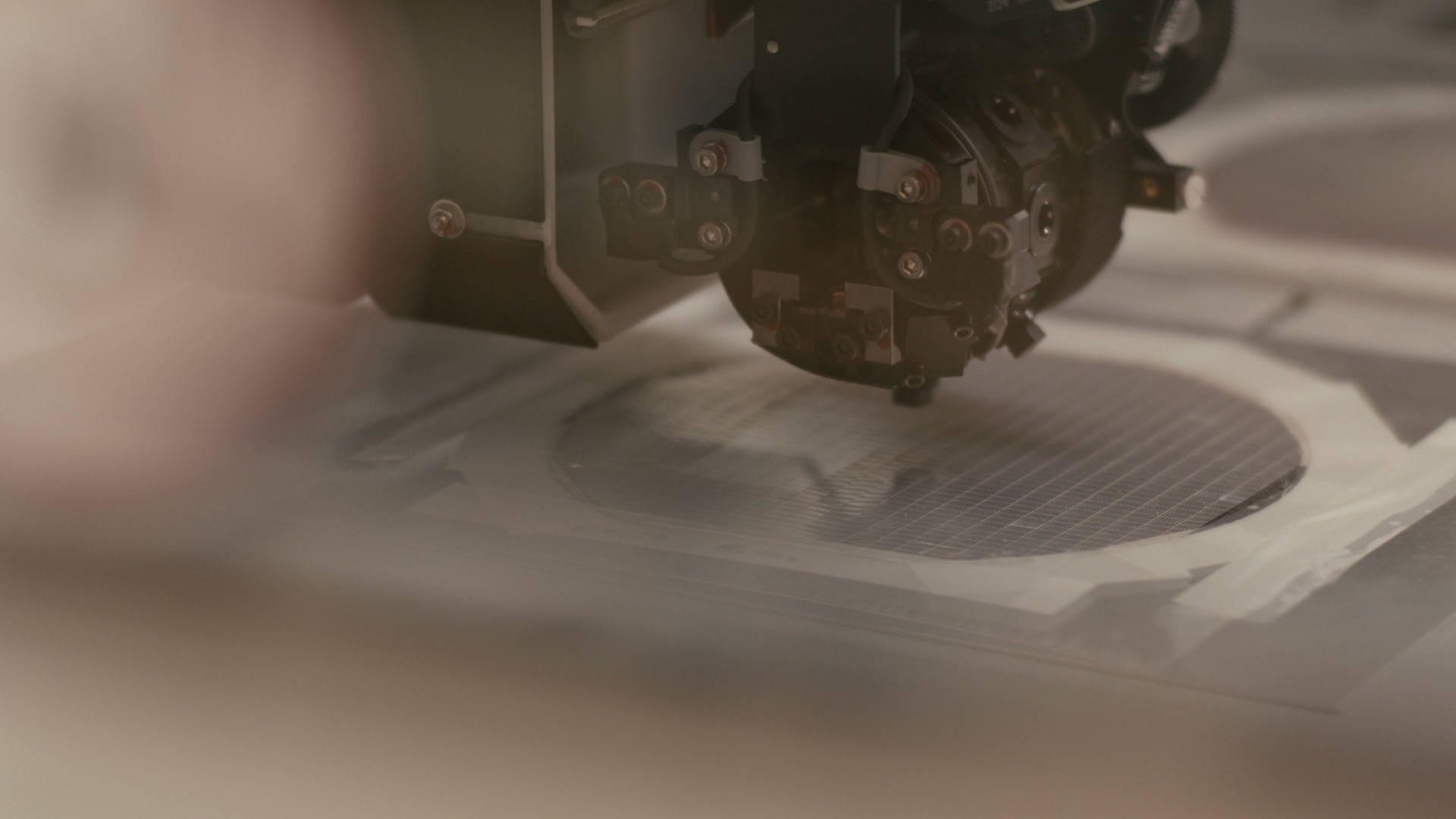 A close-up of a high-precision piece of machinery operating over a circular silicon wafer.