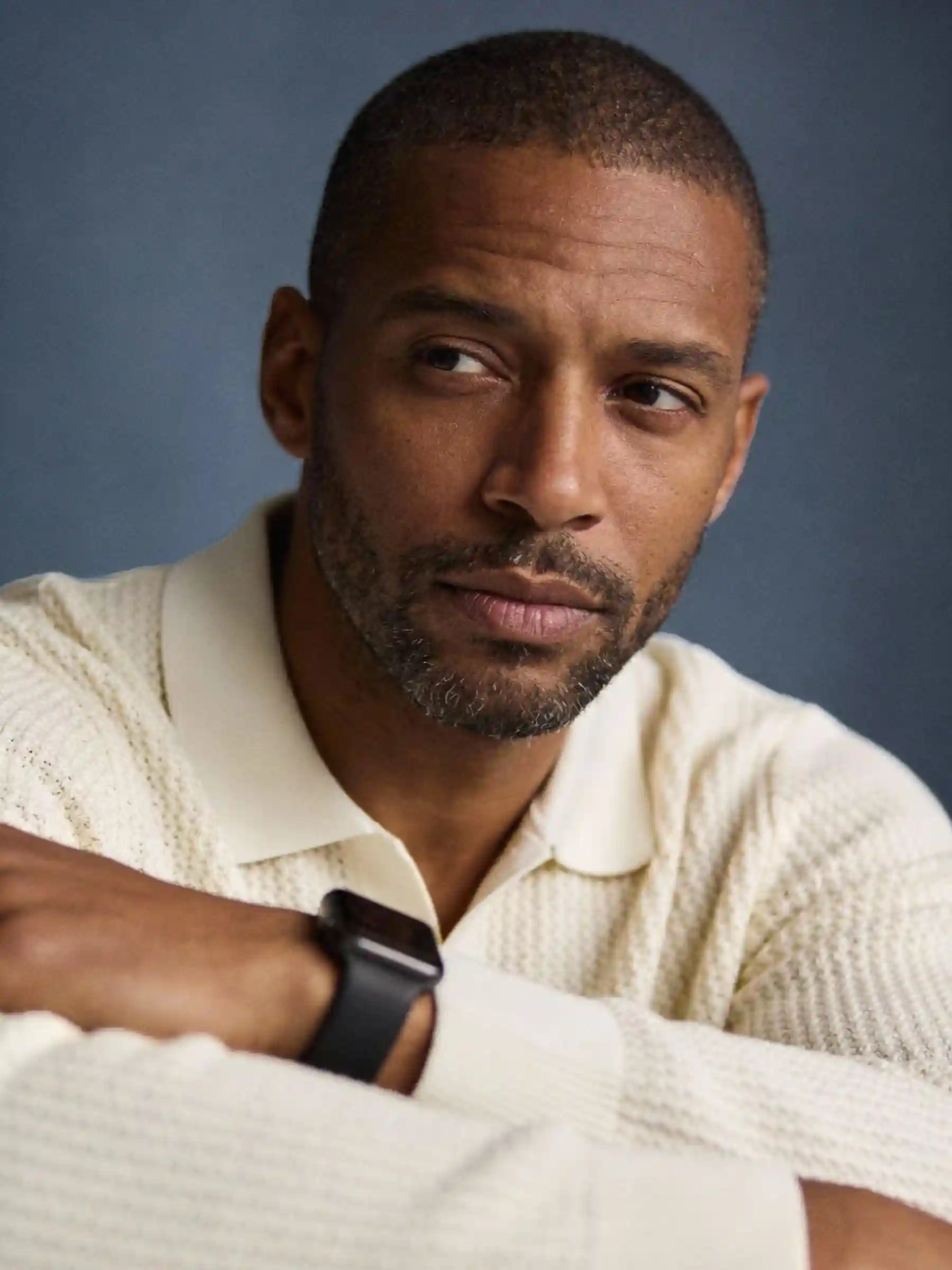 Man wearing a light sweater and a smartwatch, resting his arms and looking thoughtfully to the side.