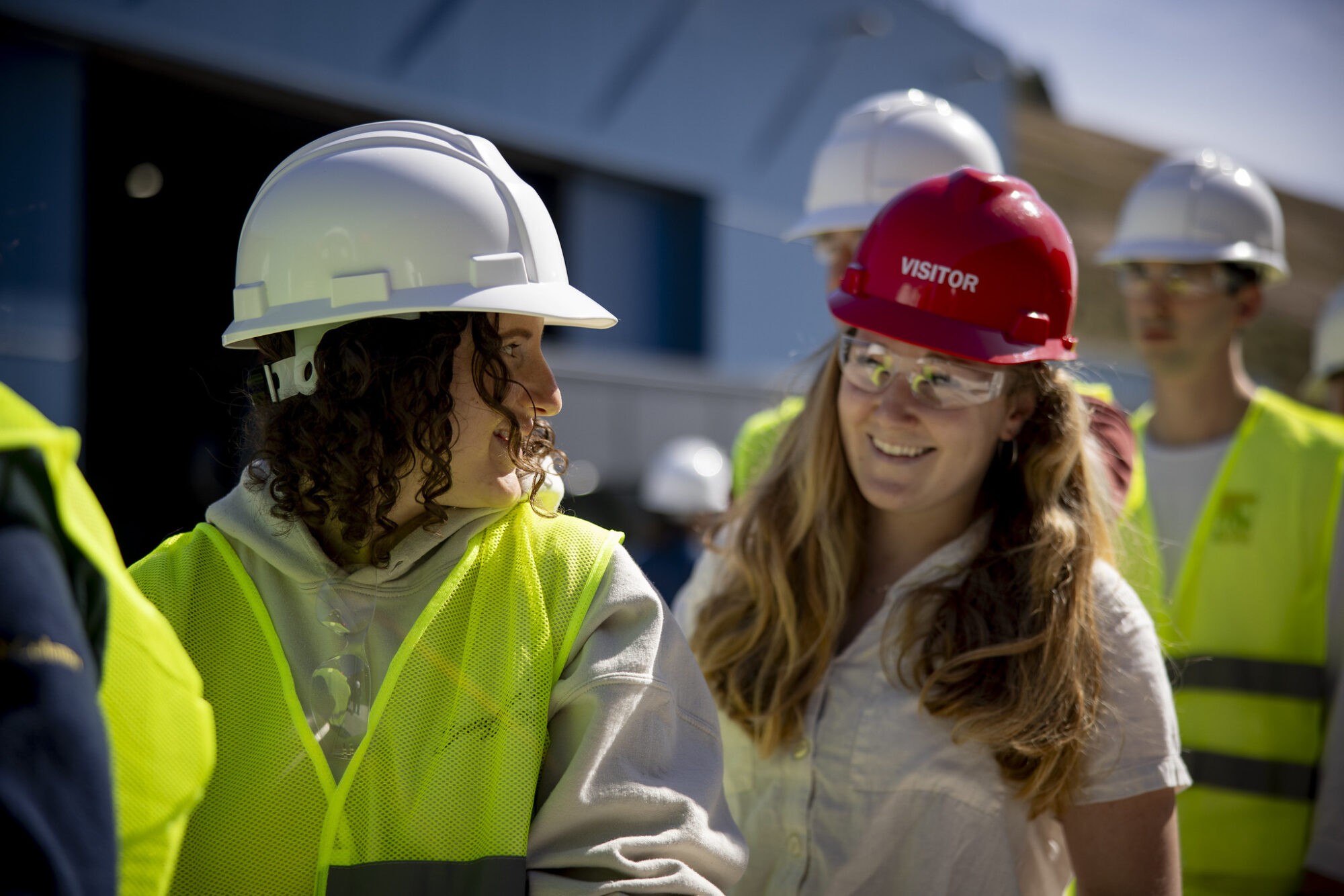 A group of construction workers is engaged in a discussion outdoors, wearing safety gear and helmets.
