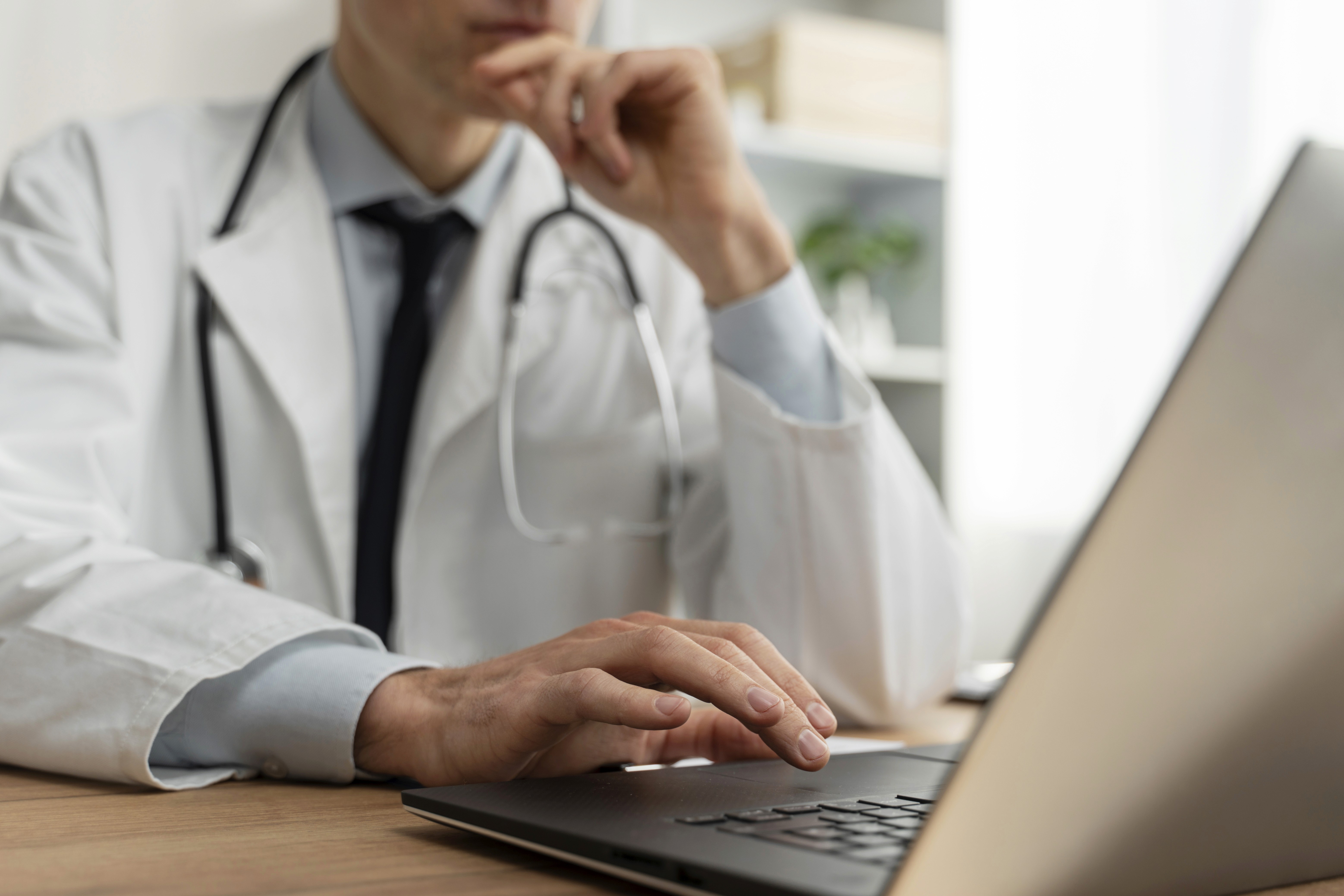 Doctor reviewing patient data on a laptop, illustrating how CompliantChatGPT helps multi-clinic networks consolidate medical records, summarize visit histories, and improve care coordination across clinics.