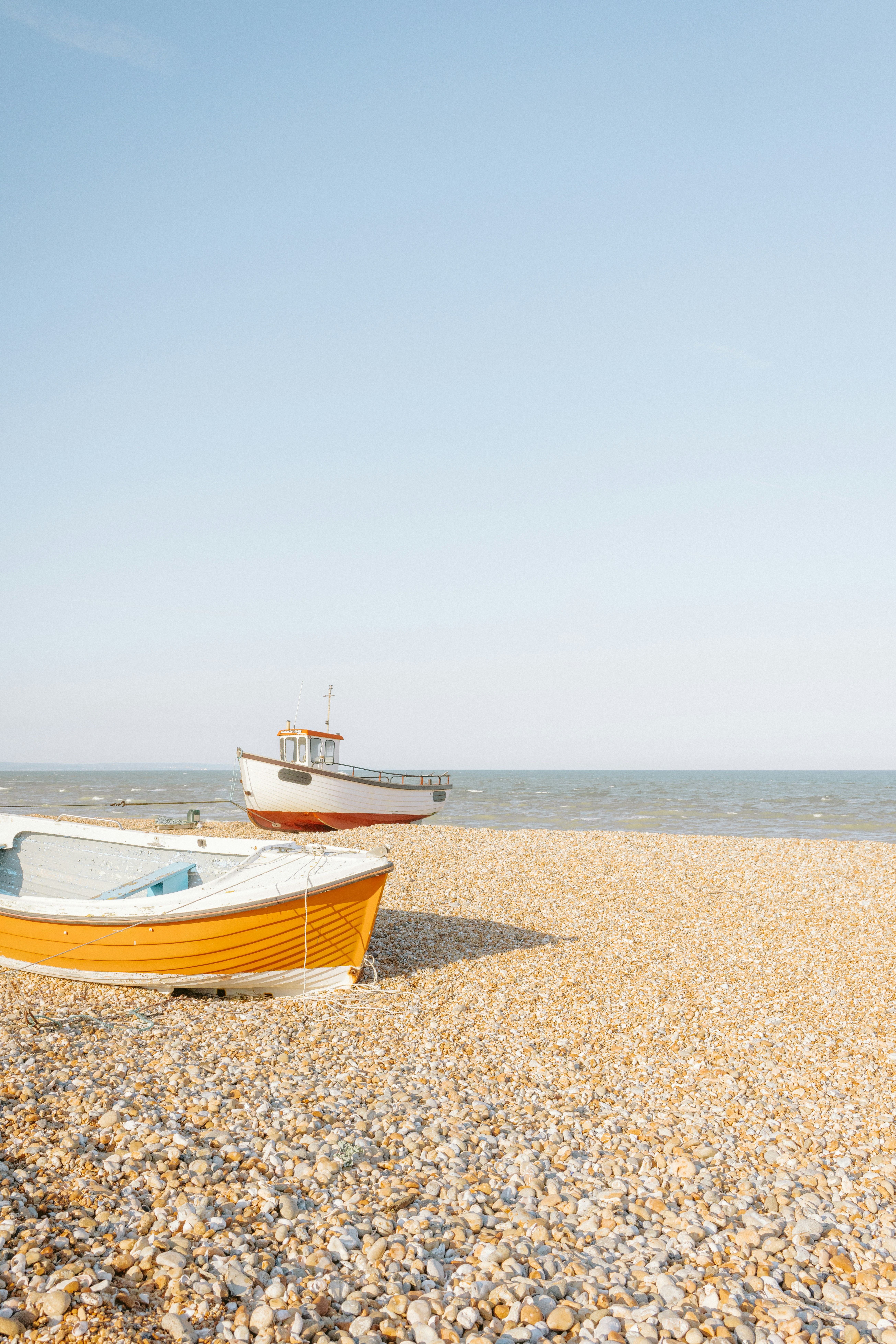 Two boats rest on a pebble beach under a clear sky.