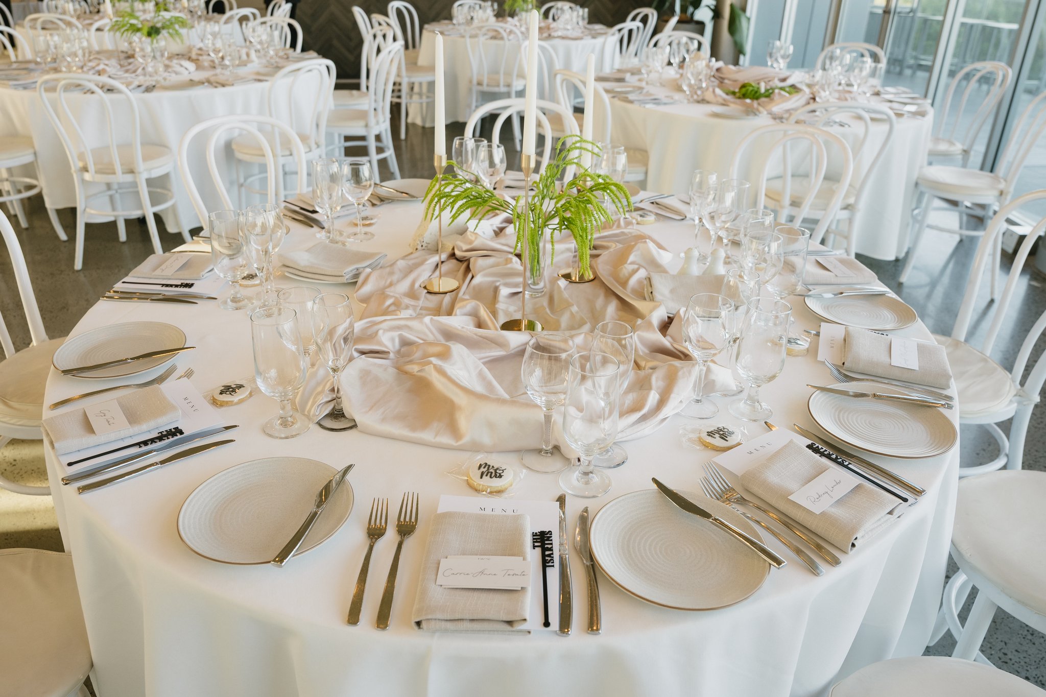 Elegant round wedding reception table set with white plates, glassware, candles and greenery centrepiece