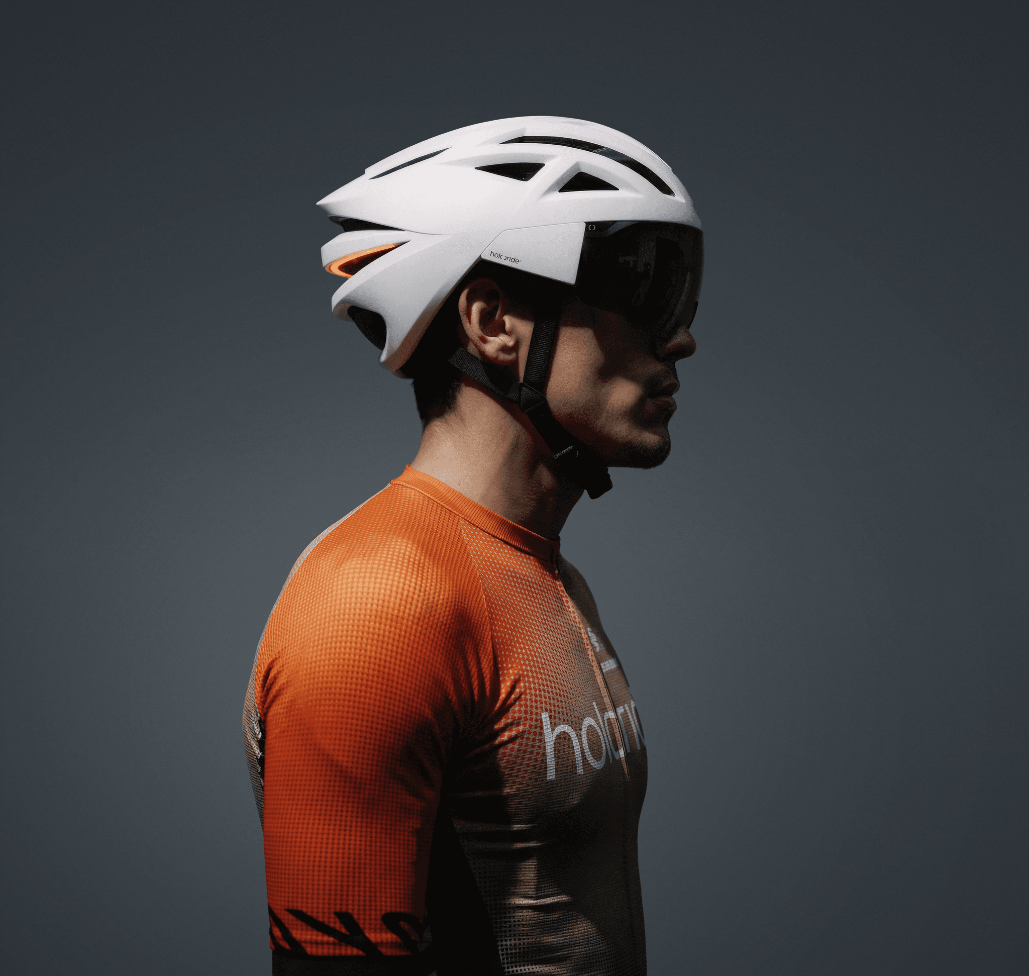 Holoride cyclist wearing a holoride helmet and branded jersey on a dark grey studio backdrop.