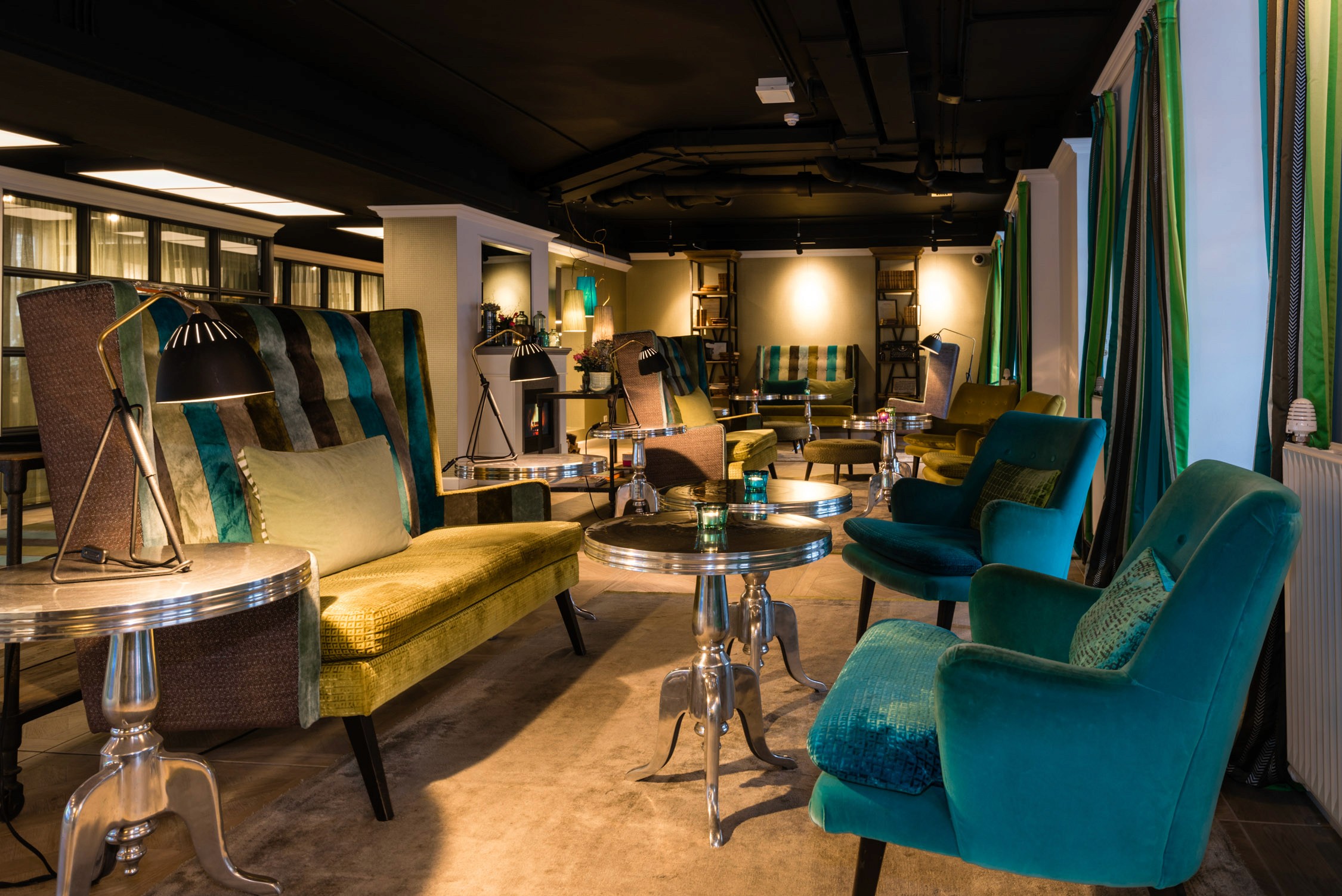 Warm ambient lighting illuminates plush seating in a stylish lounge featuring deep teal and mustard yellow accents.