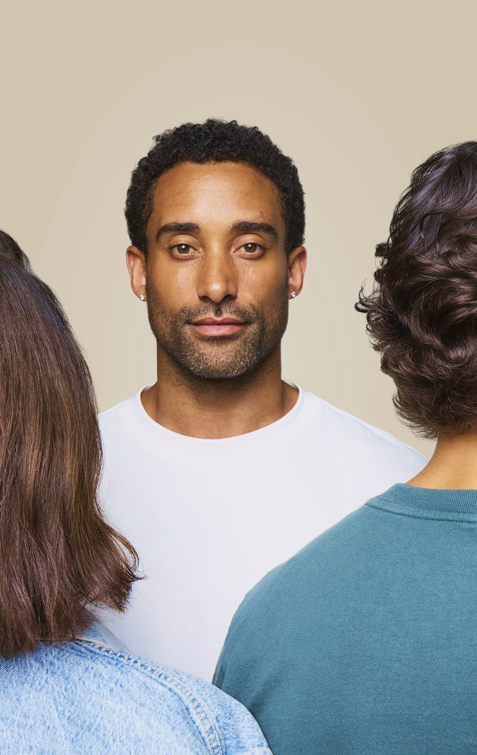 A man stands in front, looking at the camera, while three people face away from him, engaged in conversation.