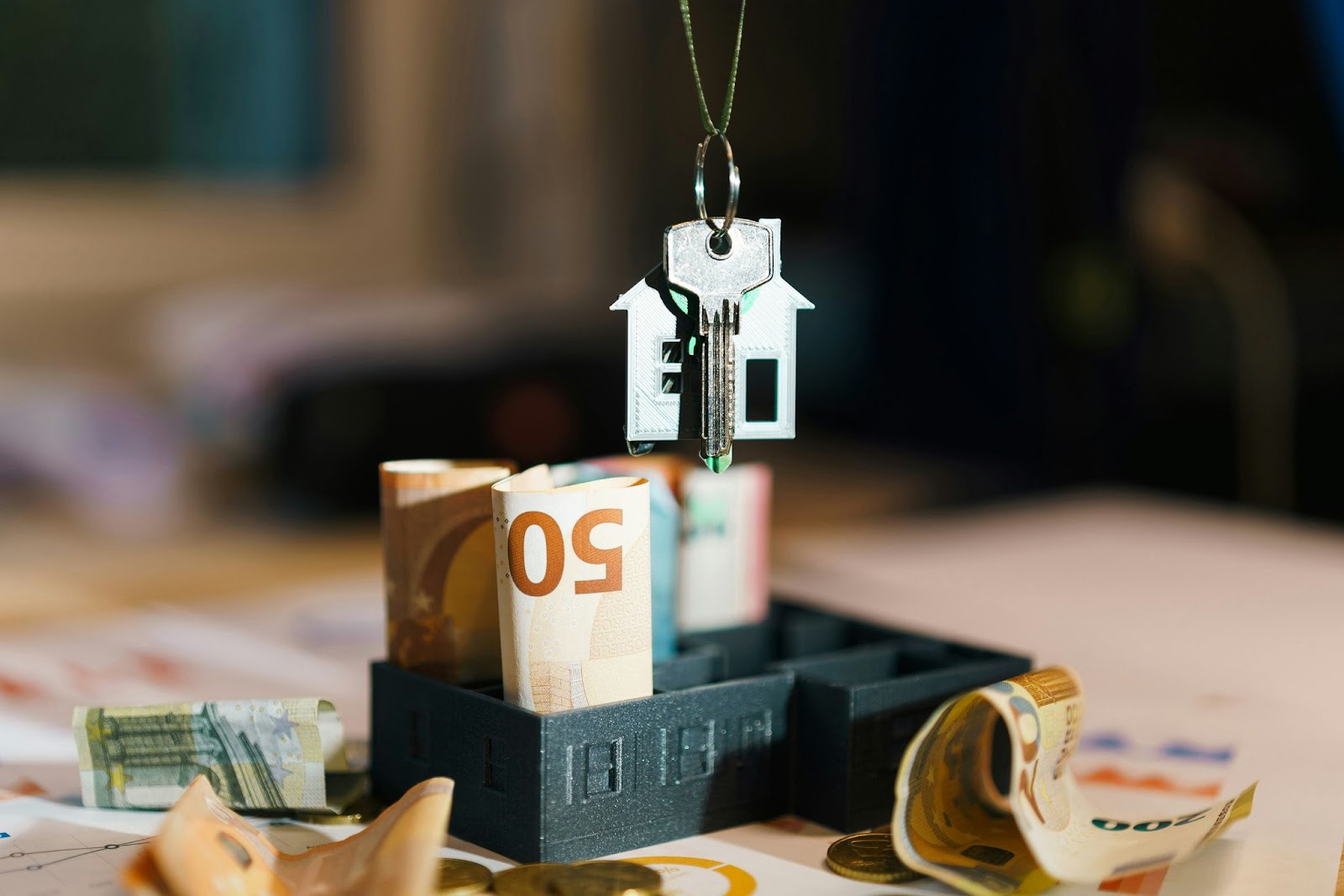 A house and key on a keychain above a desk with European bills