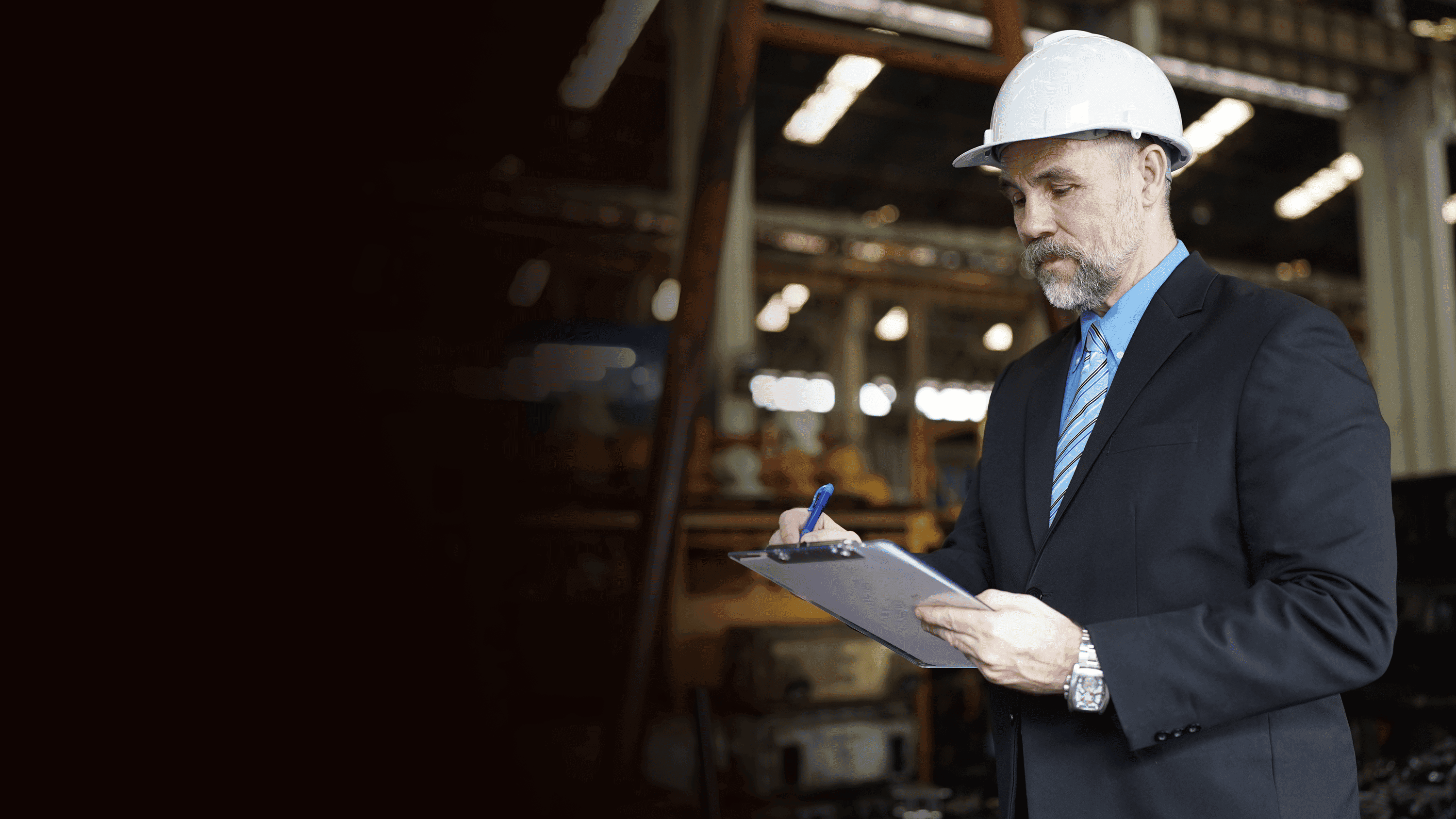 Gestor vestindo terno e gravata utilizando um capacete e com uma caderneta na mão fazendo avaliações.