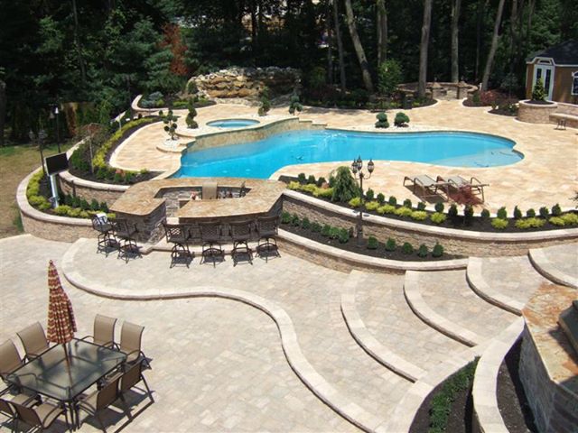 Multi-level stone patio with in-ground pool and curved seating walls