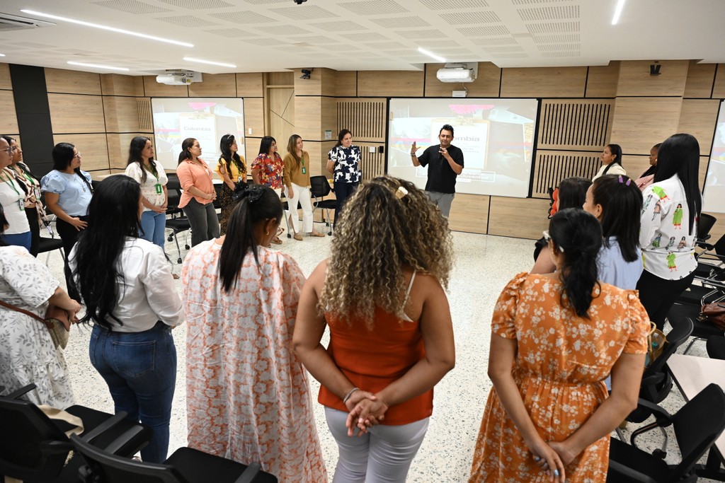 Jorge Baena en una dinámica grupal, hablando con un grupo de mujeres en un salón mientras todos están de pie en círculo.