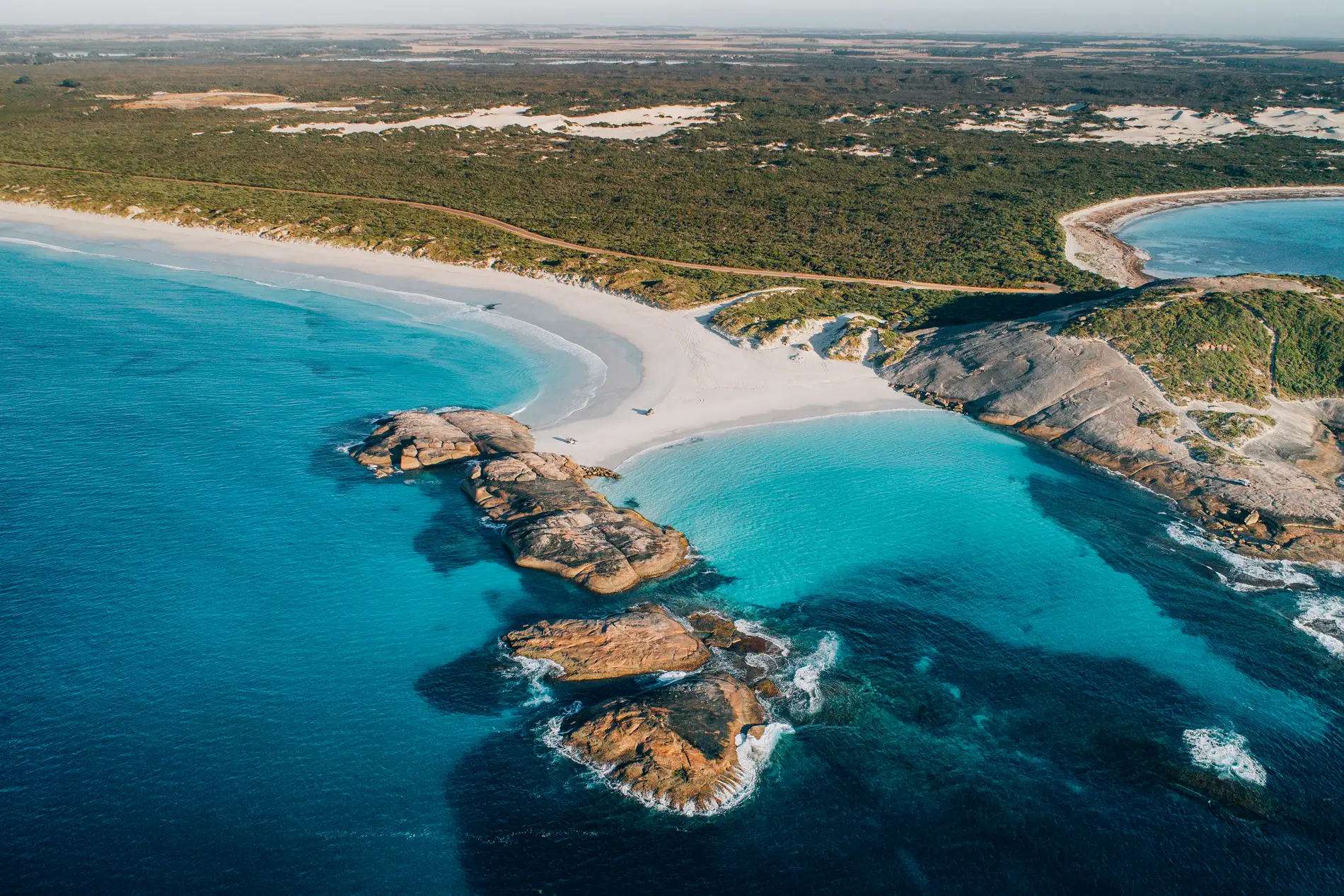Aerial of granite islets in a turquoise bay beside a curving white beach