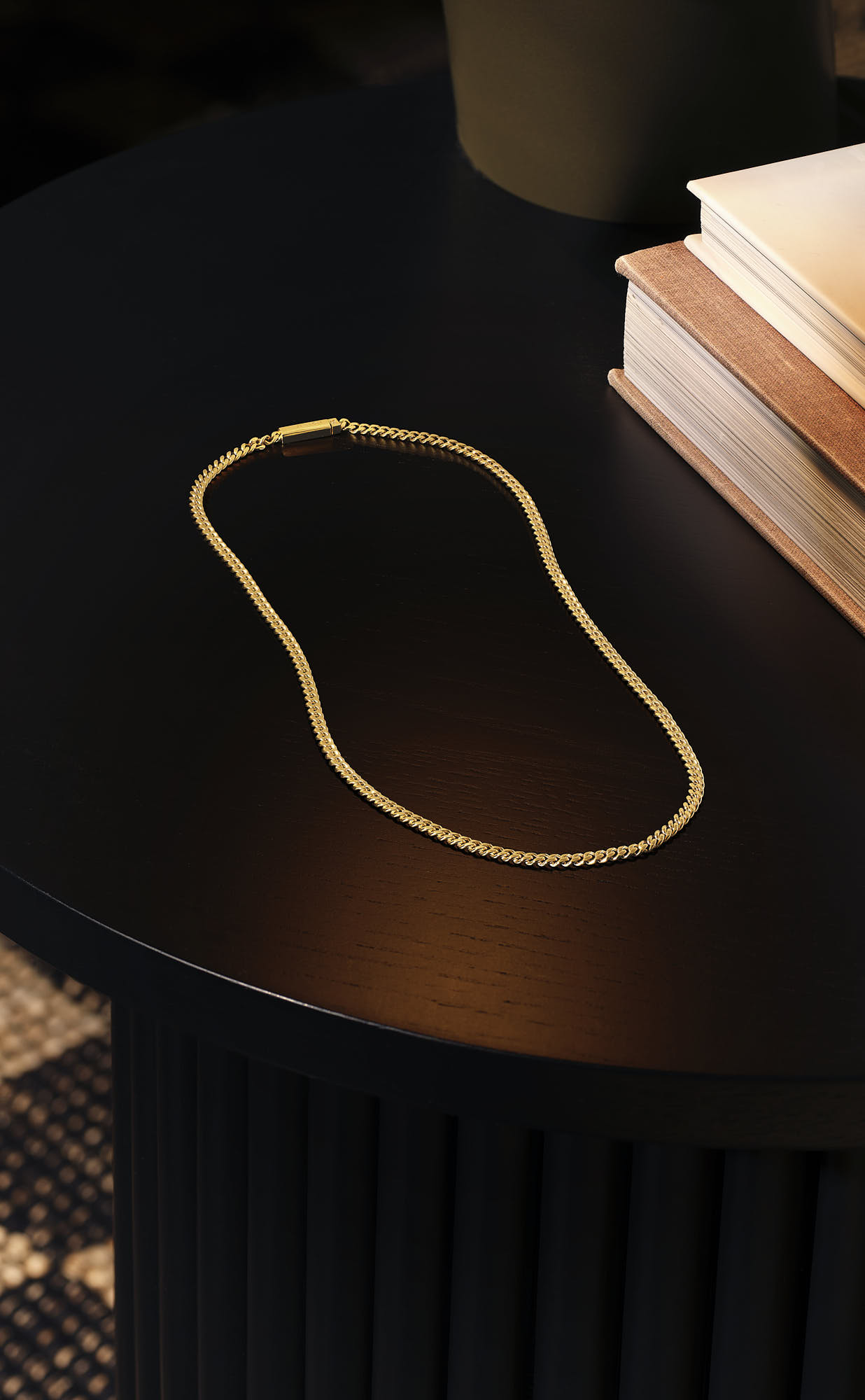 Elegant gold chain necklace on black table near stacked books.