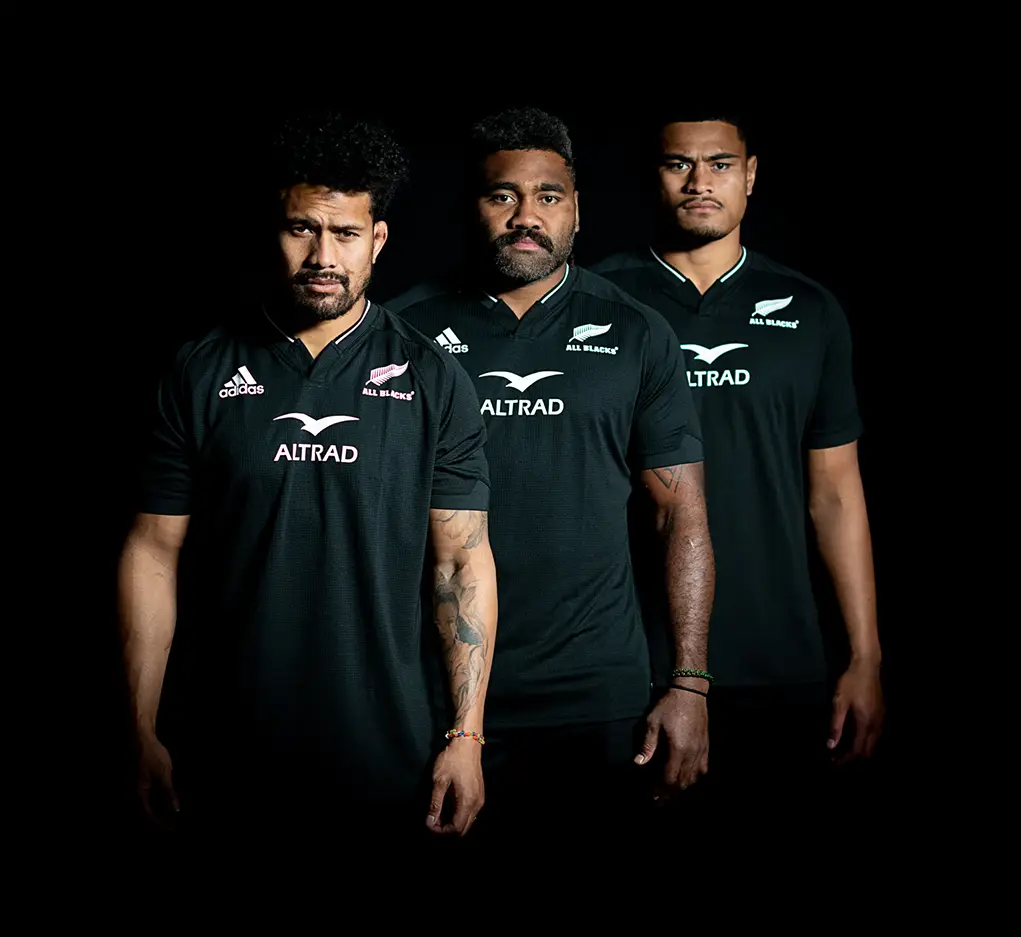 Three New Zealand All Black Rugby Players look at the camera in a dark environment