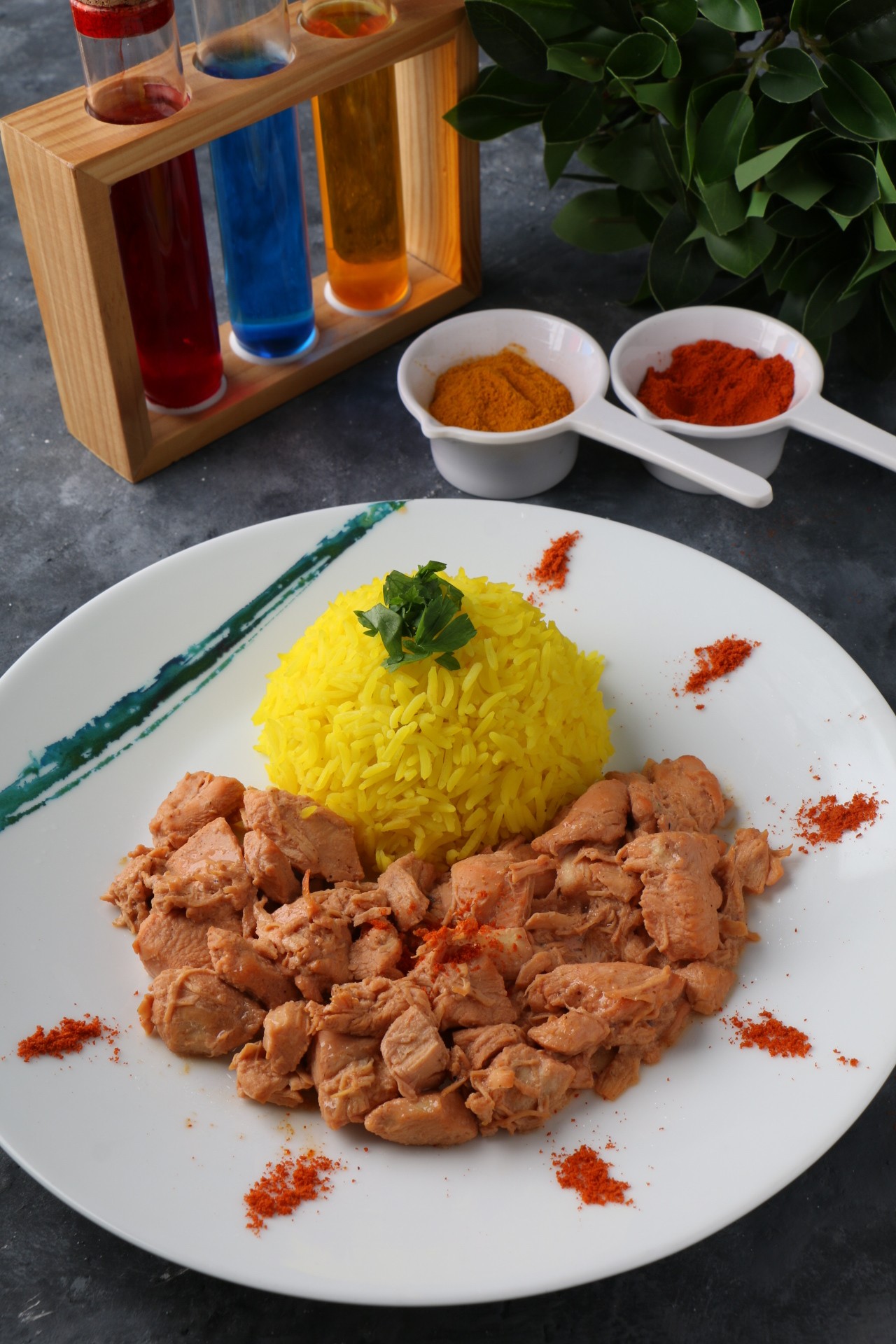 A close-up of a dark gray bowl filled with white fish chunks, cherry tomatoes, green olives, and herbs, served next to a glass of white wine on a white table by a window.