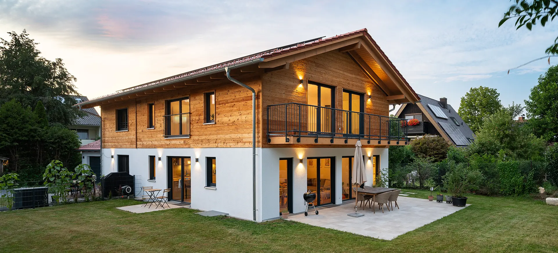 Modernes zweistöckiges Haus mit Holzfassade im Obergeschoss und weiß verputztem Erdgeschoss, umgeben von Garten und Nachbarhäusern