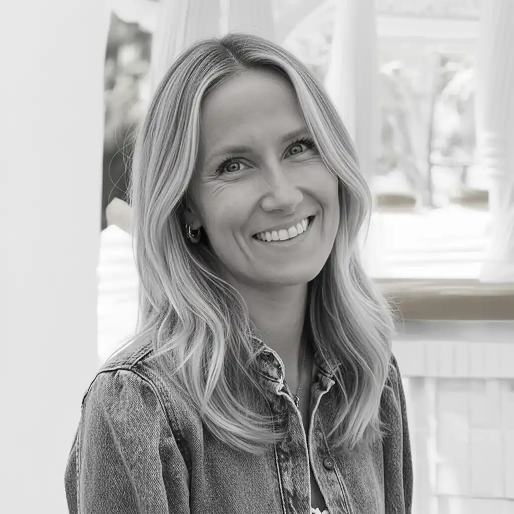 Et svart-hvitt portrett av en smilende kvinne med lyst, halvlangt hår, kledd i en denimskjorte.