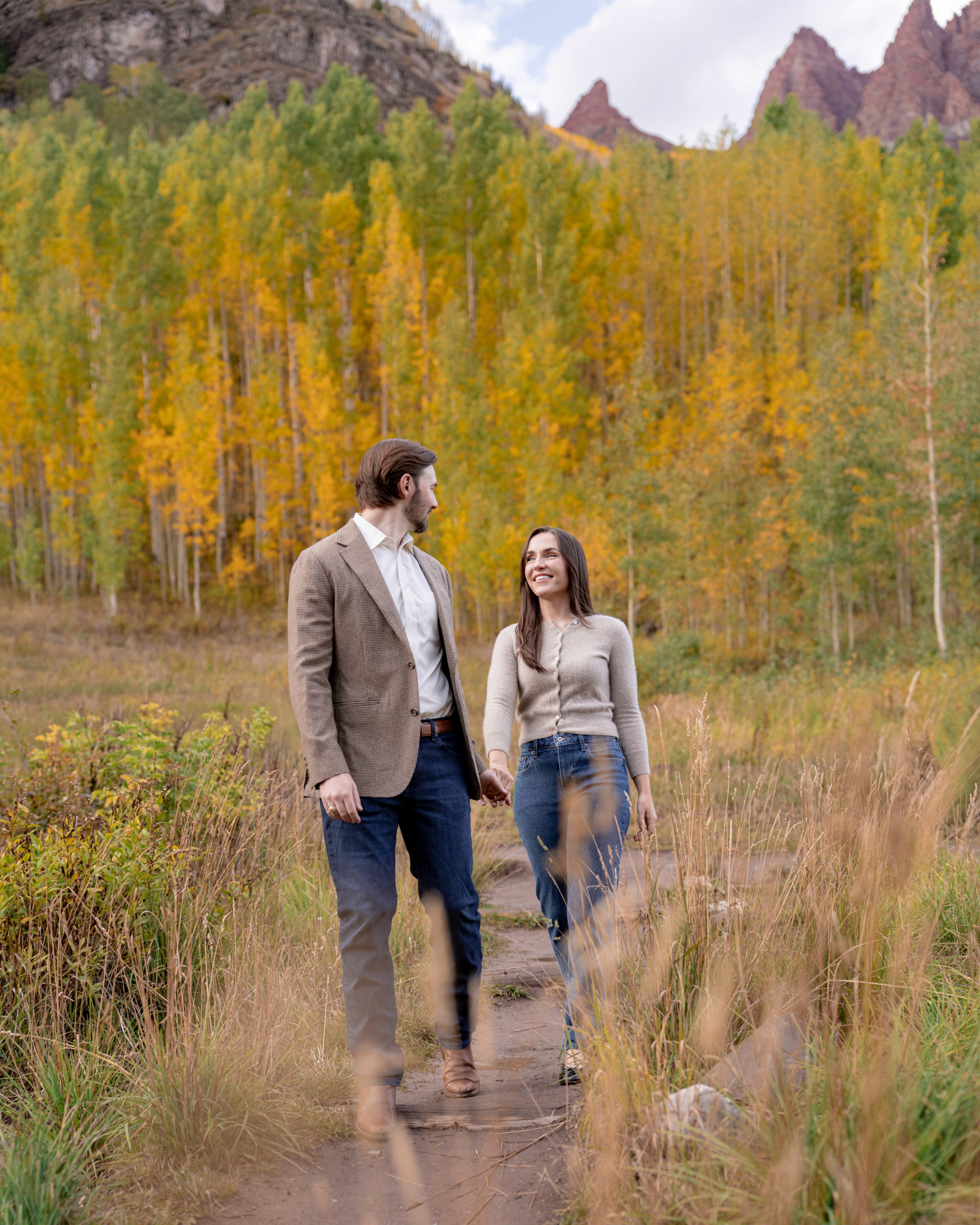 Tim and Lexi walk hand in hand along a path beneath golden aspen trees.