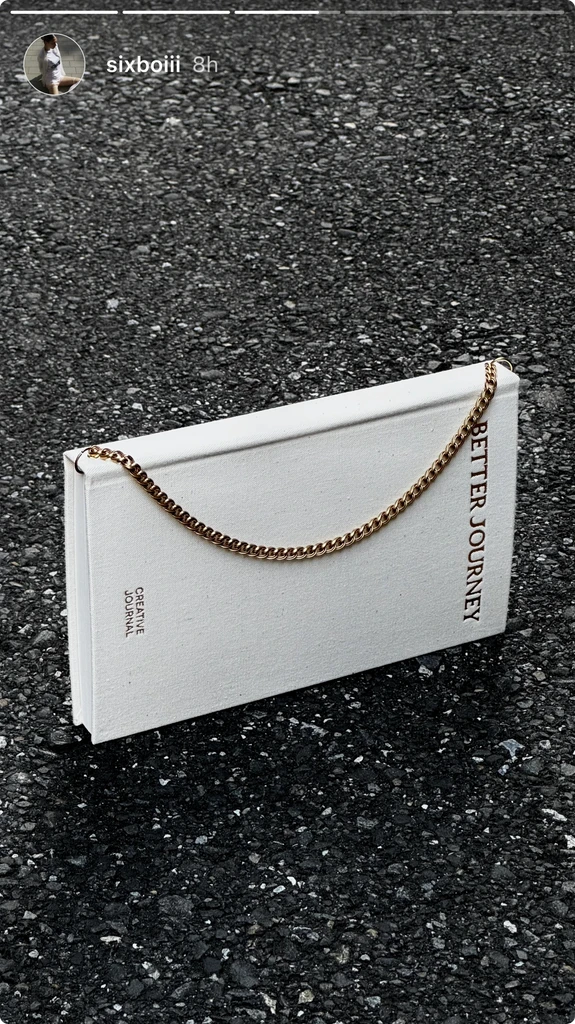 White BETTER JOURNEY Creative Journal with brass chain bookmark lying on textured ground, highlighting its minimalist design and unique features