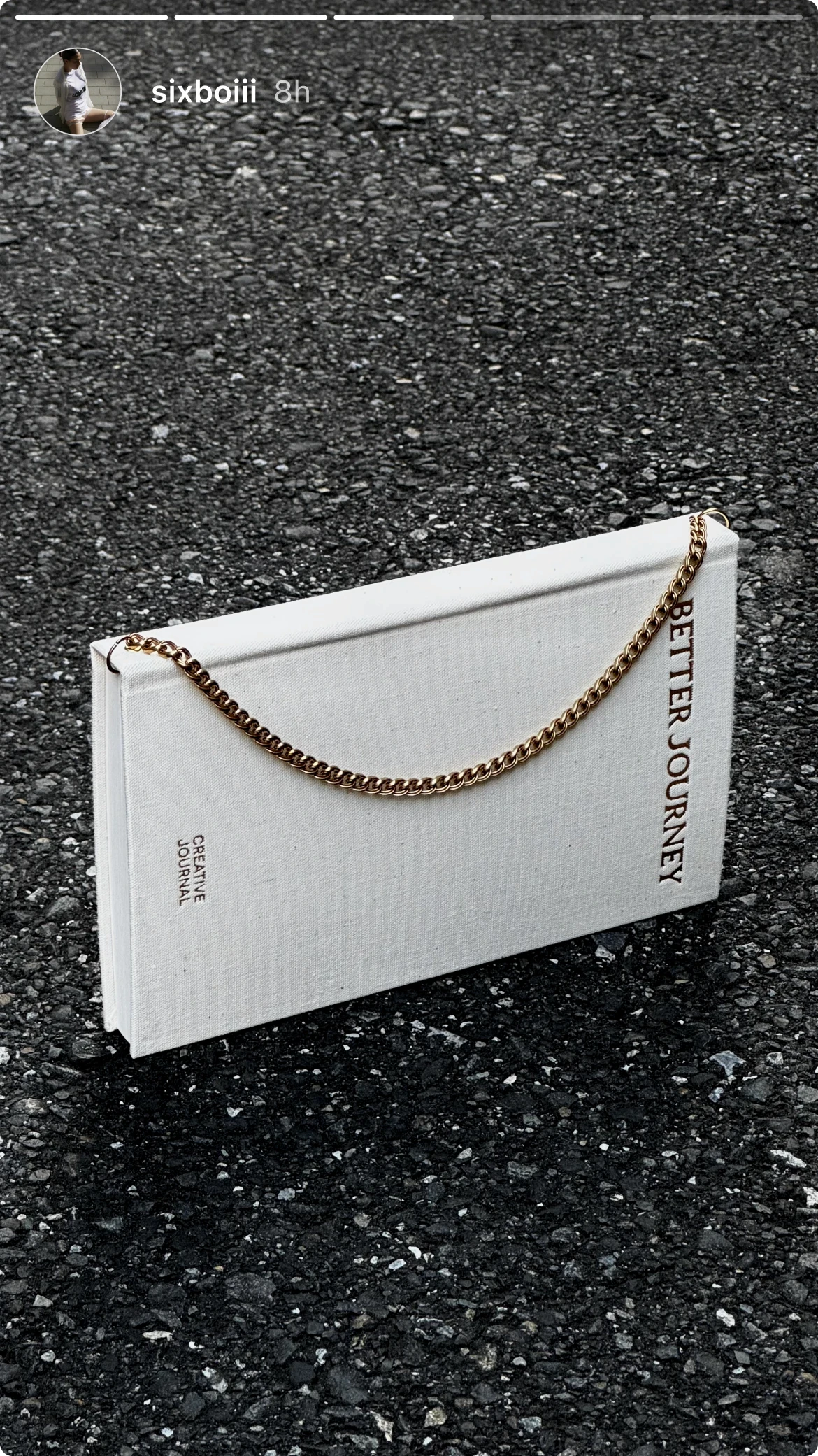 White BETTER JOURNEY Creative Journal with brass chain bookmark lying on textured ground, highlighting its minimalist design and unique features