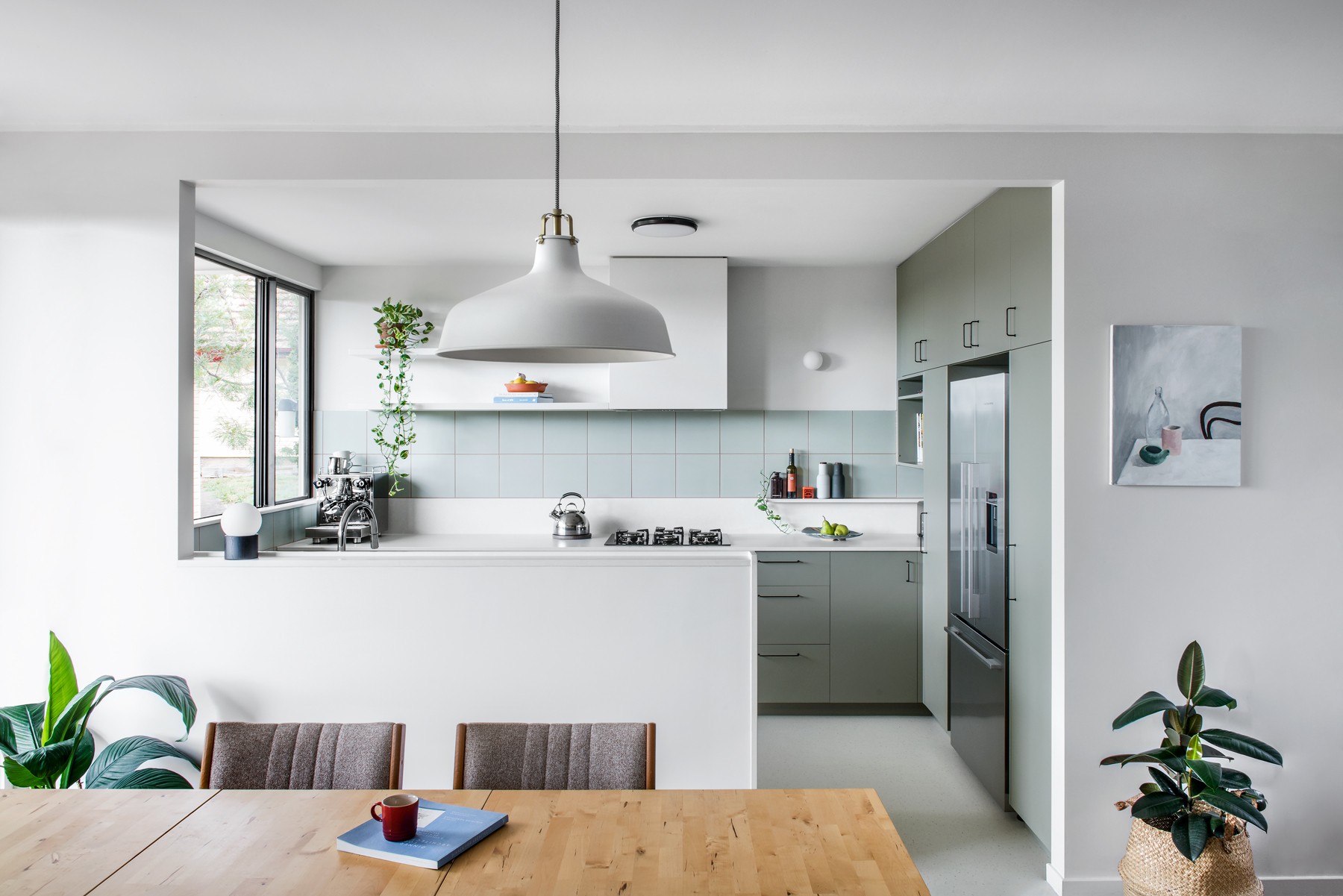 Wide view of Glenhaven Kitchen from the dining area, with muted green cabinetry, a central island, pendant lighting, and soft daylight connecting the kitchen to the adjoining living space.