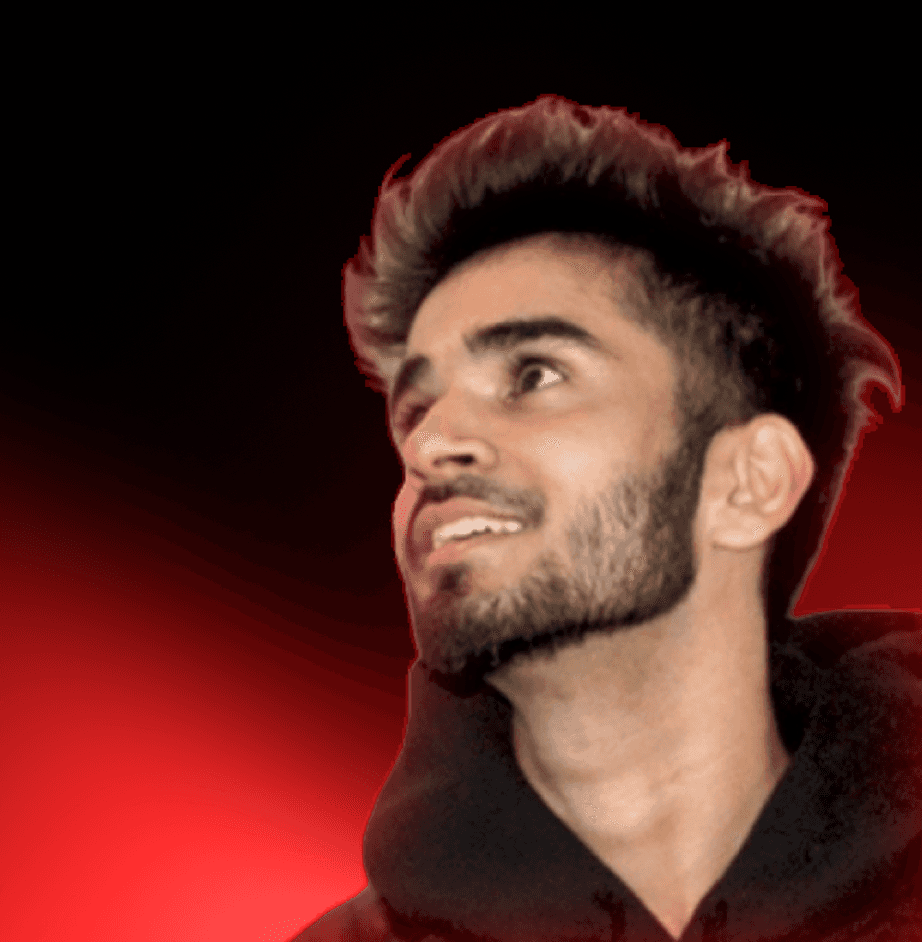 A man with a beard wears a black jacket over a dark shirt, smiling in front of a softly illuminated background.