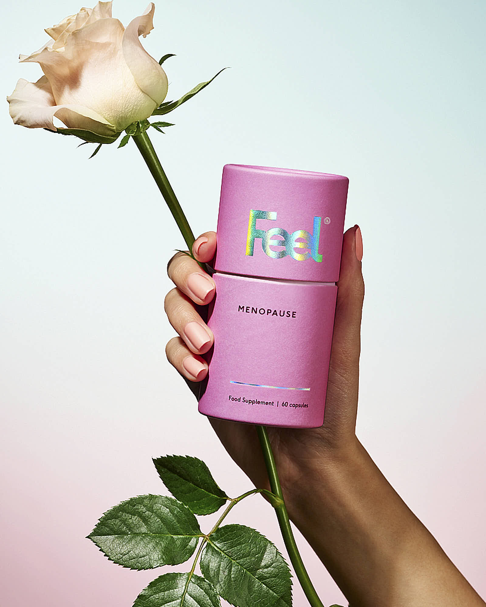A hand holds a pink can next to a rose, set against a soft pastel background.