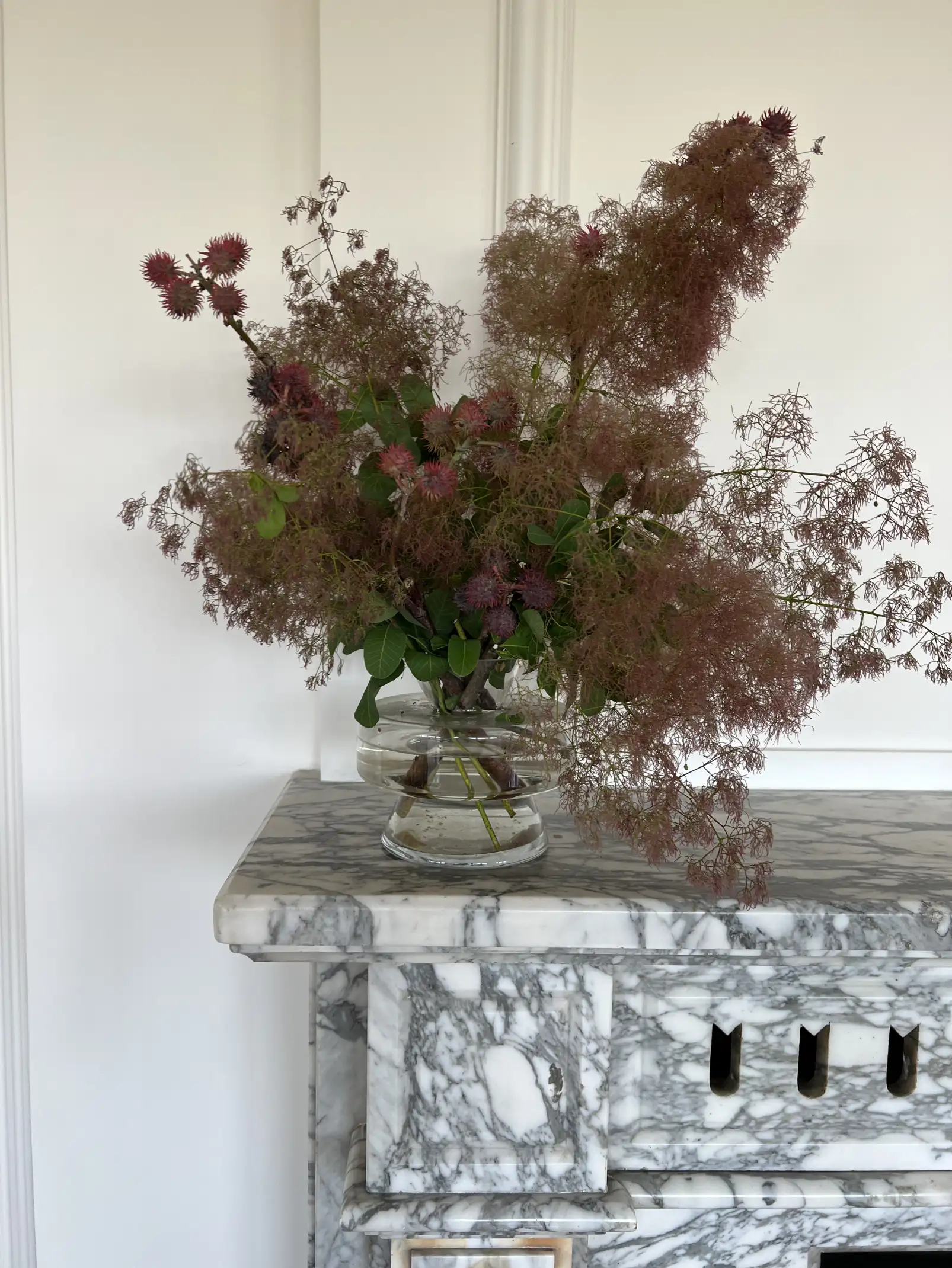 Arreglo floral con follaje rosado sobre chimenea de mármol para espacios clásicos que integran arte botánico y elegancia atemporal.