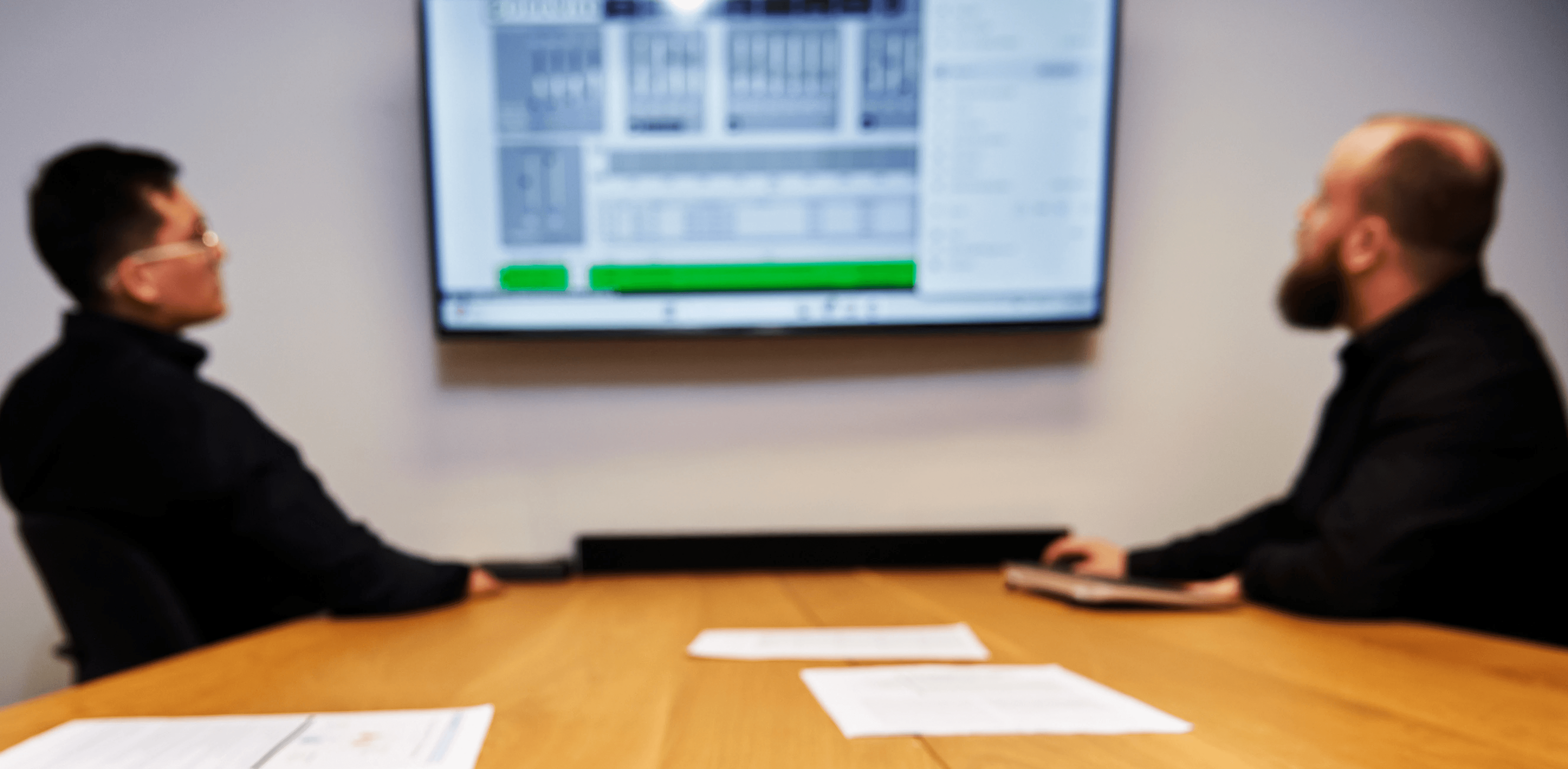 Black and white image of people working at a table with laptops, showing hands gesturing during discussion of digital content displayed on screens, with fabrica® logo in the corner.