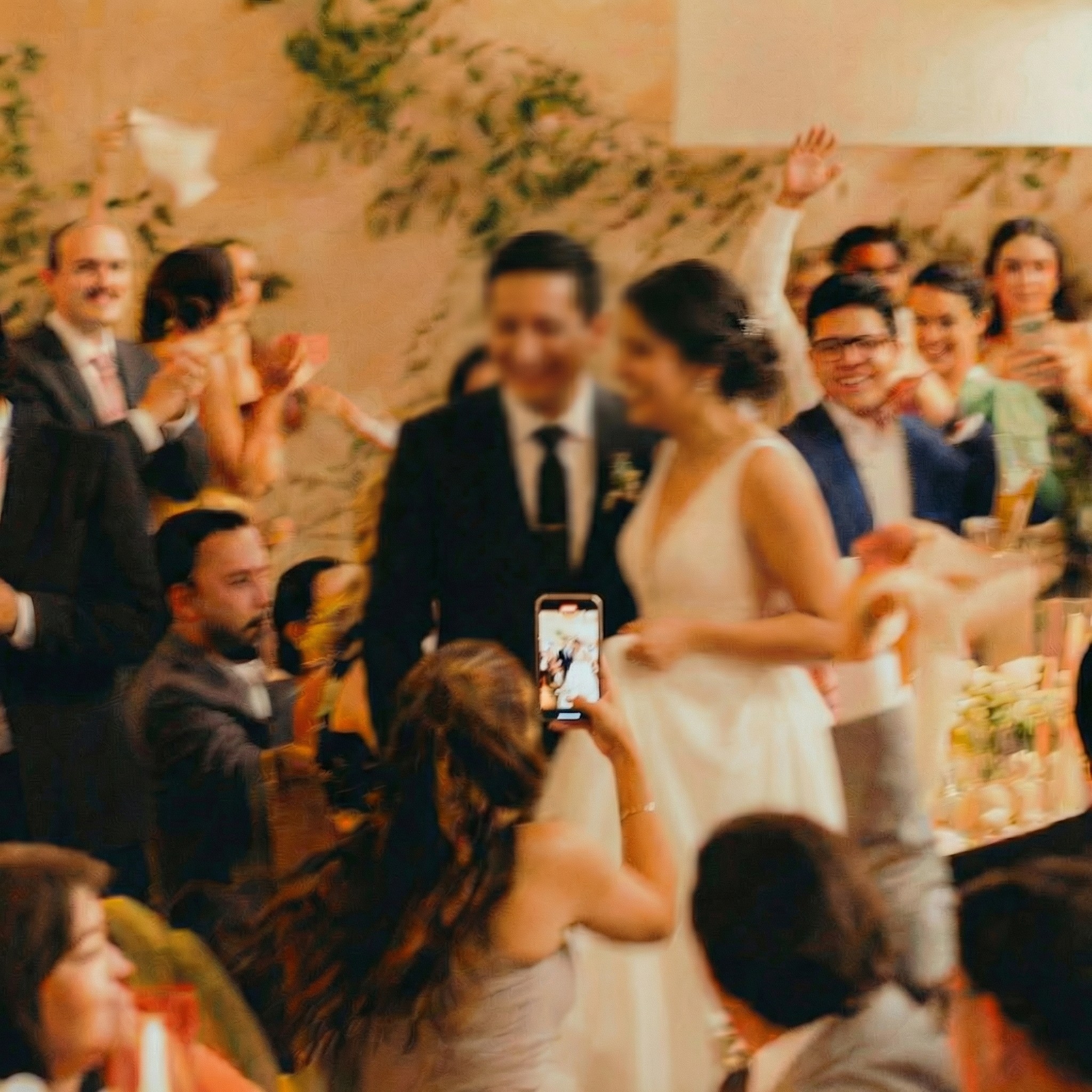 A couple dances closely, showcasing a flowing green dress, against a soft, blurred background of other guests.