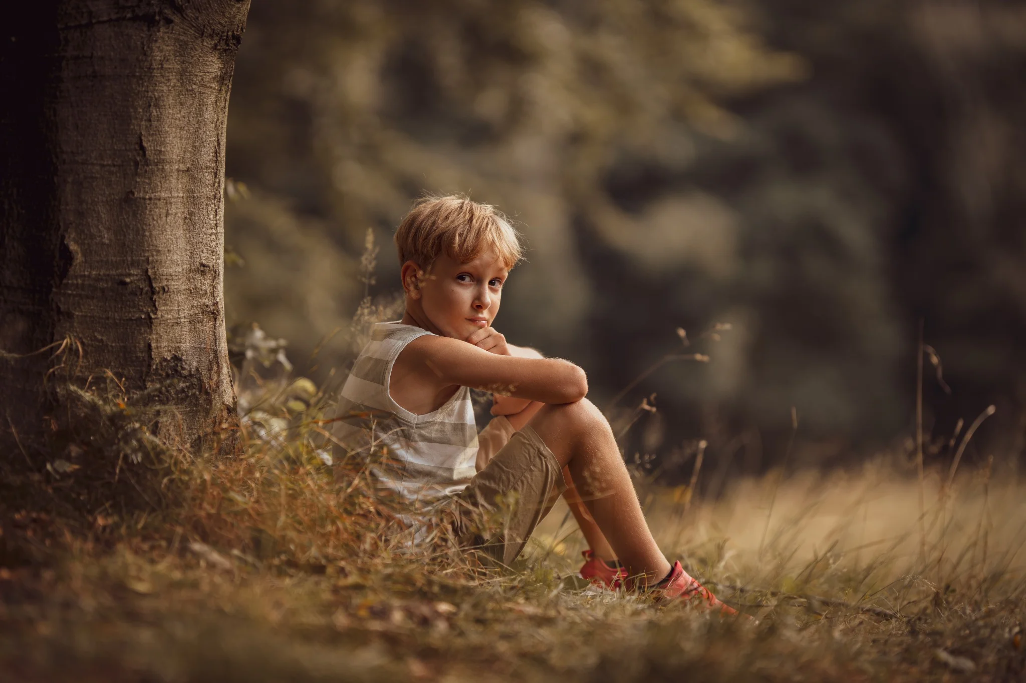 Na zdjęciu znajduje się niemowlę leżące na białym kocu. Dziecko ma na sobie szarą, dzianinową czapkę i patrzy prosto w kamerę. Tło jest rozmyte, co sprawia, że cała uwaga skupia się na twarzy dziecka. Światło jest miękkie, co nadaje zdjęciu ciepły i przytulny charakter.