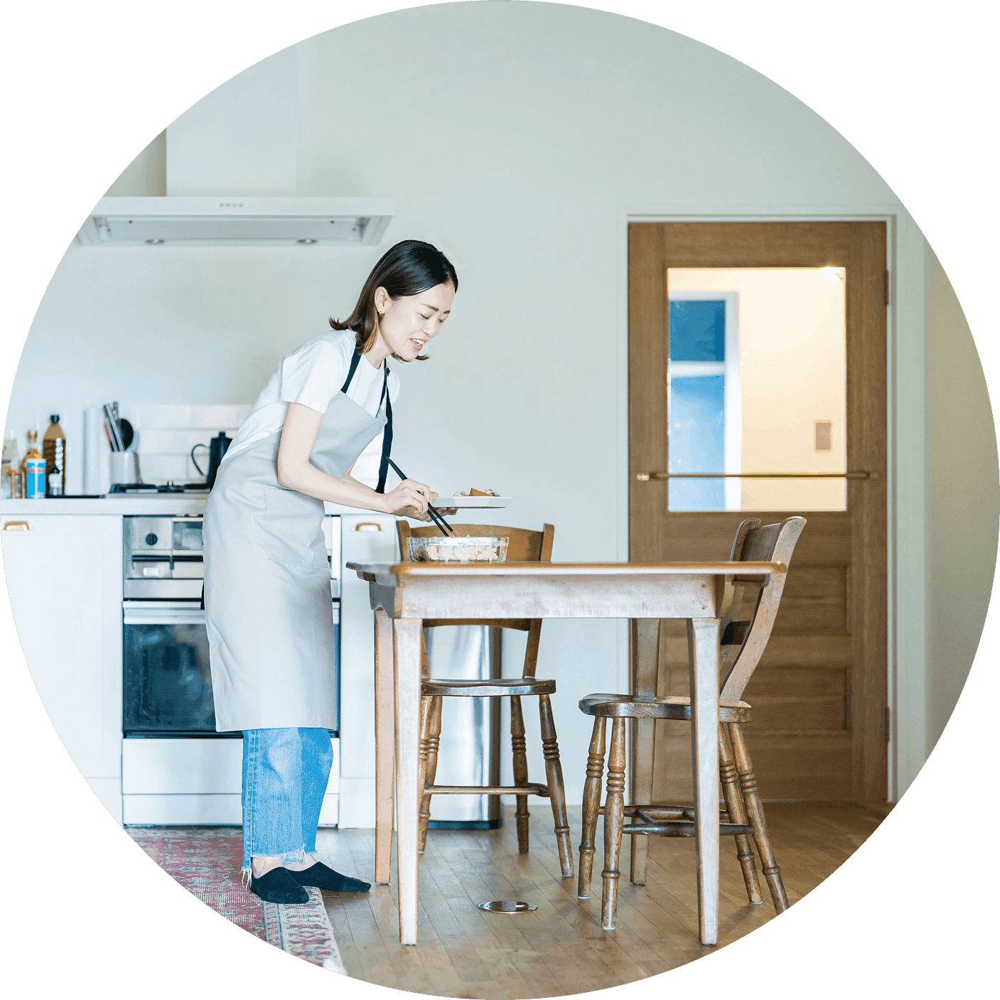 Woman in an apron sets a dish on a dining table in a bright home kitchen