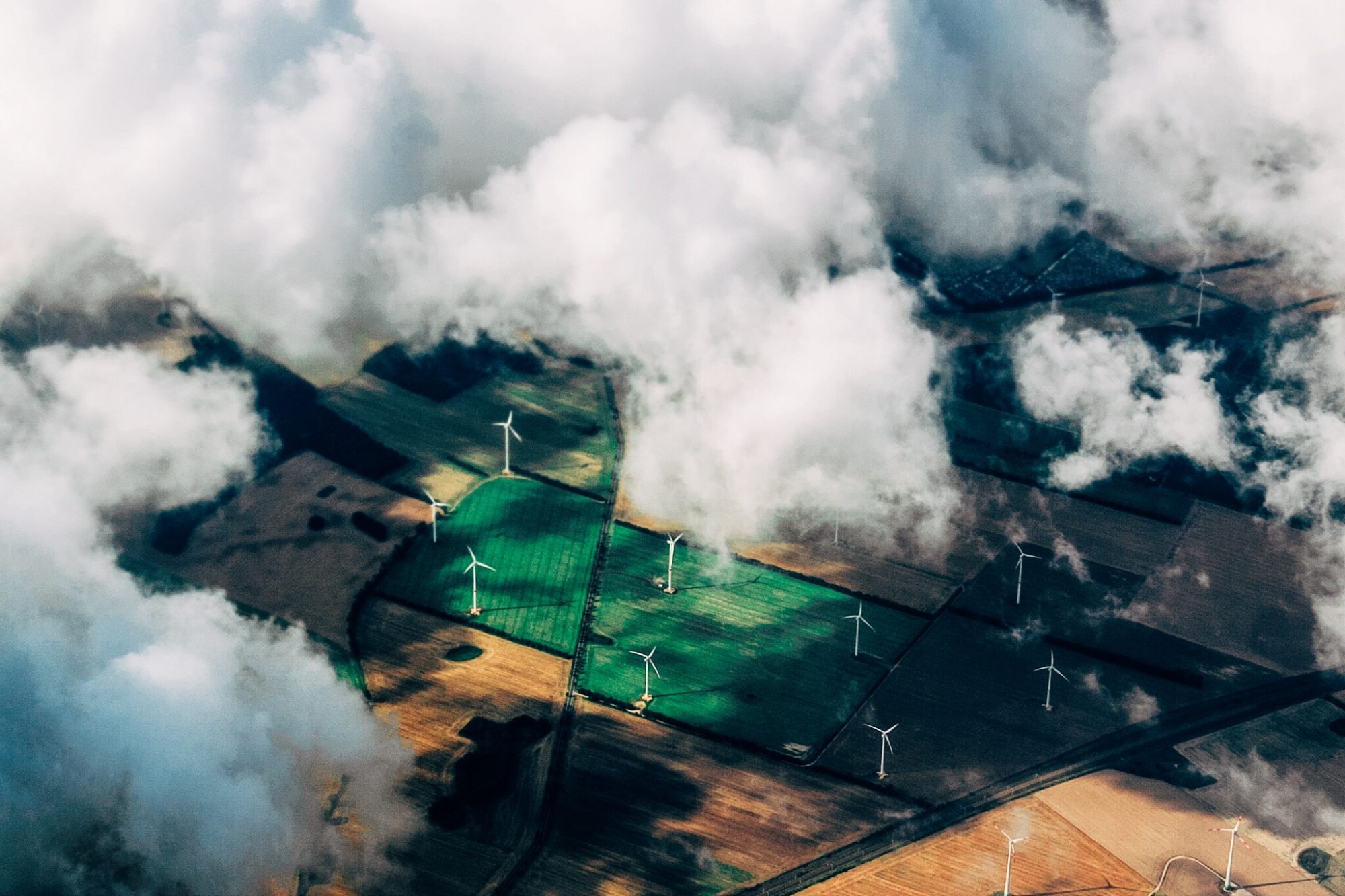 Aerial view of lush green landscapes peeking through fluffy white clouds.
