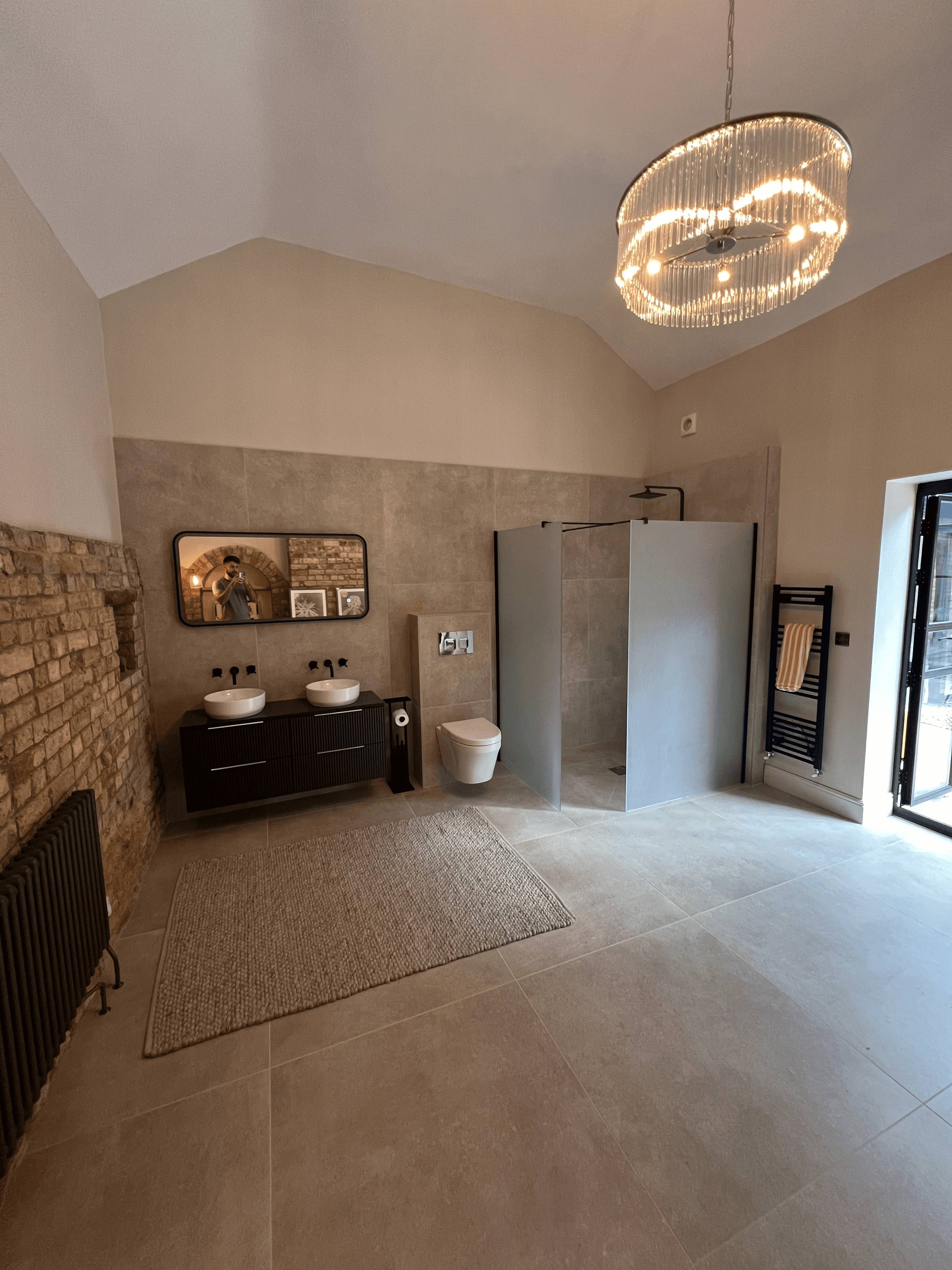 Spacious modern bathroom featuring exposed brick walls, double vanity, a walk-in shower, and a statement chandelier, completed by PPM Builders.