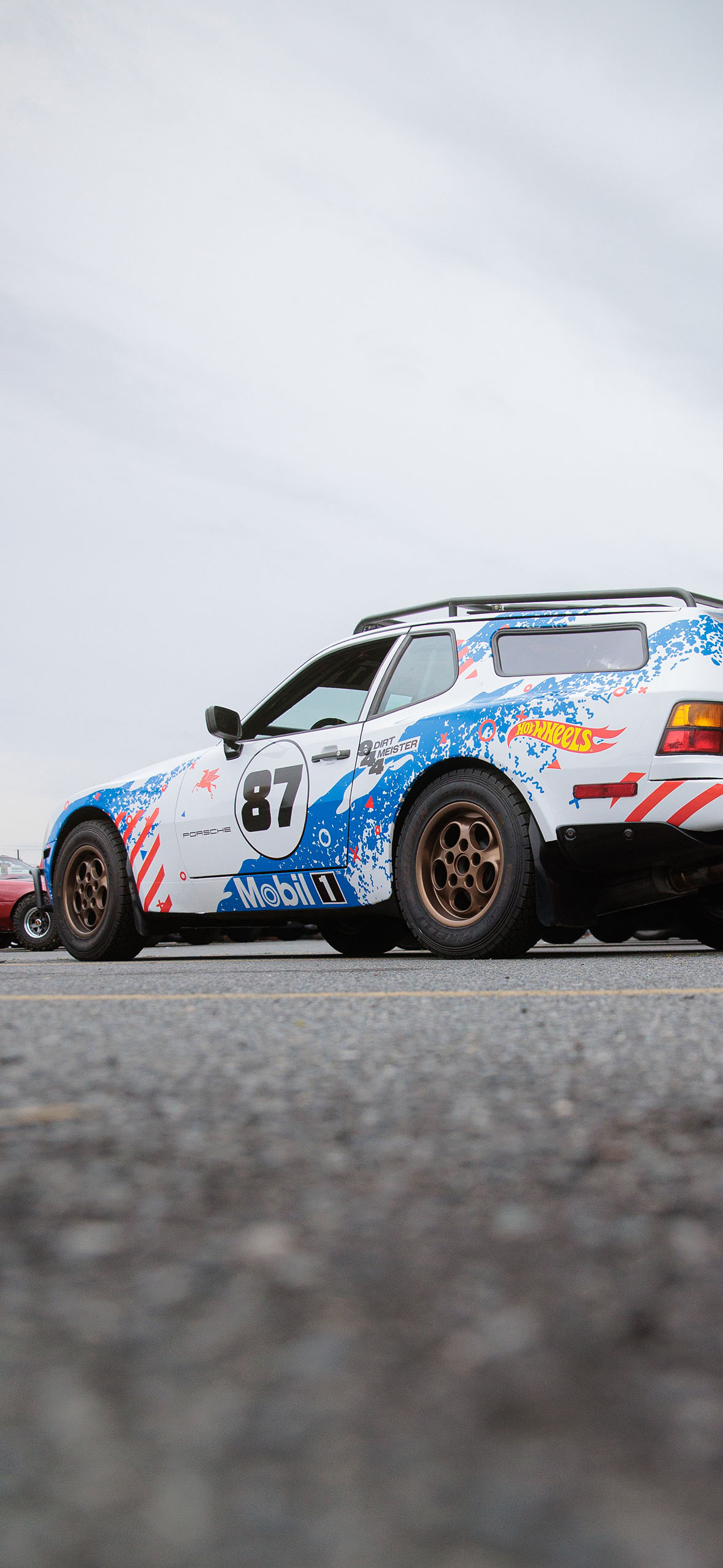 White and blue Porsche 911 with the number 87, parked in a parking lot.