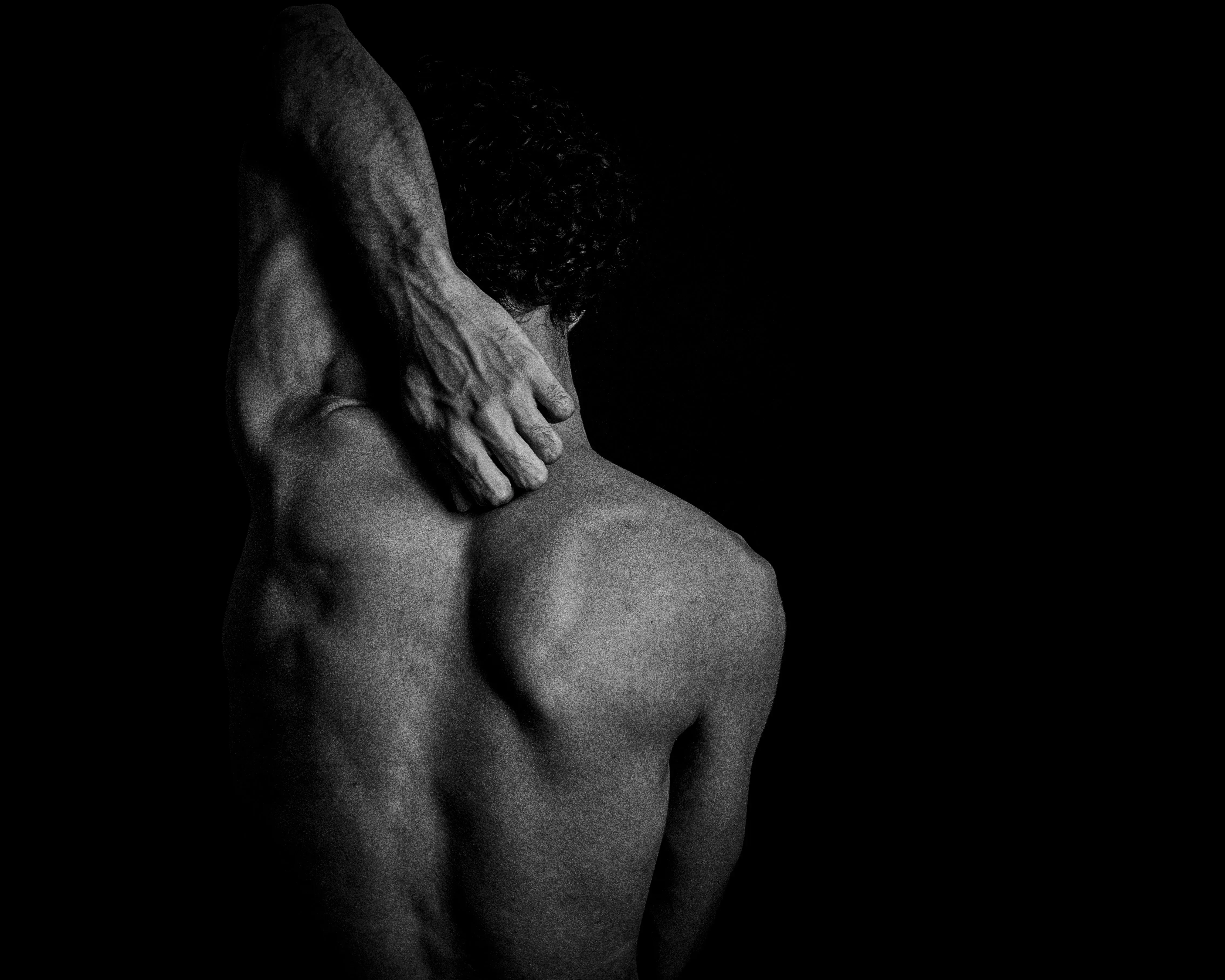 A dark, artistic photograph of a person's back, with one hand resting on the shoulder.