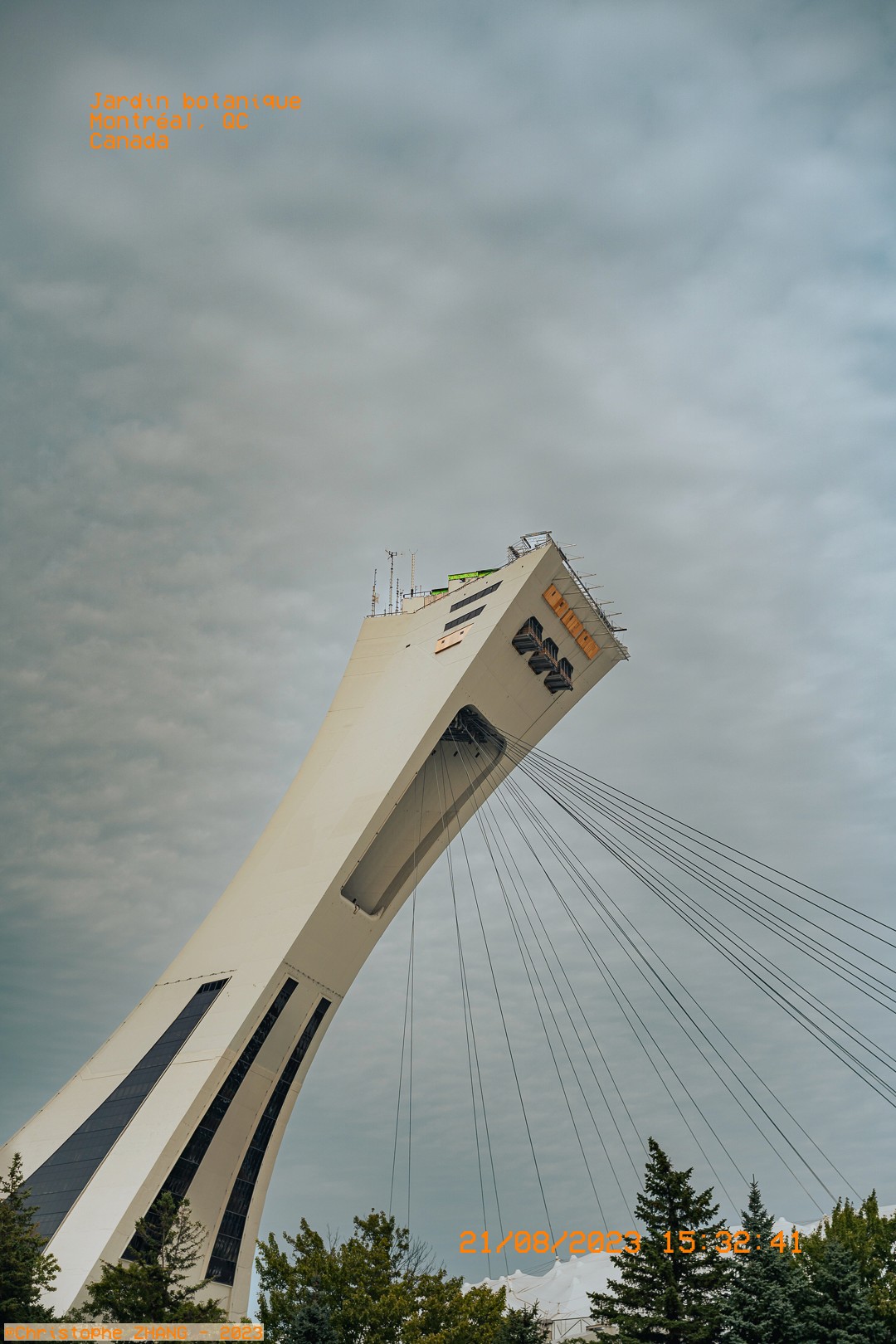Vue rapprochée de la tour inclinée du Stade olympique sous un ciel nuageux.