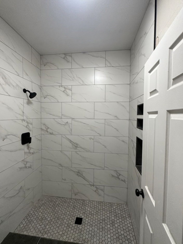 Elegant shower enclosure with white marble-look rectangular wall tiles, a light hexagonal mosaic shower floor, and dark shower fixtures, showcasing a sleek and clean tile design.