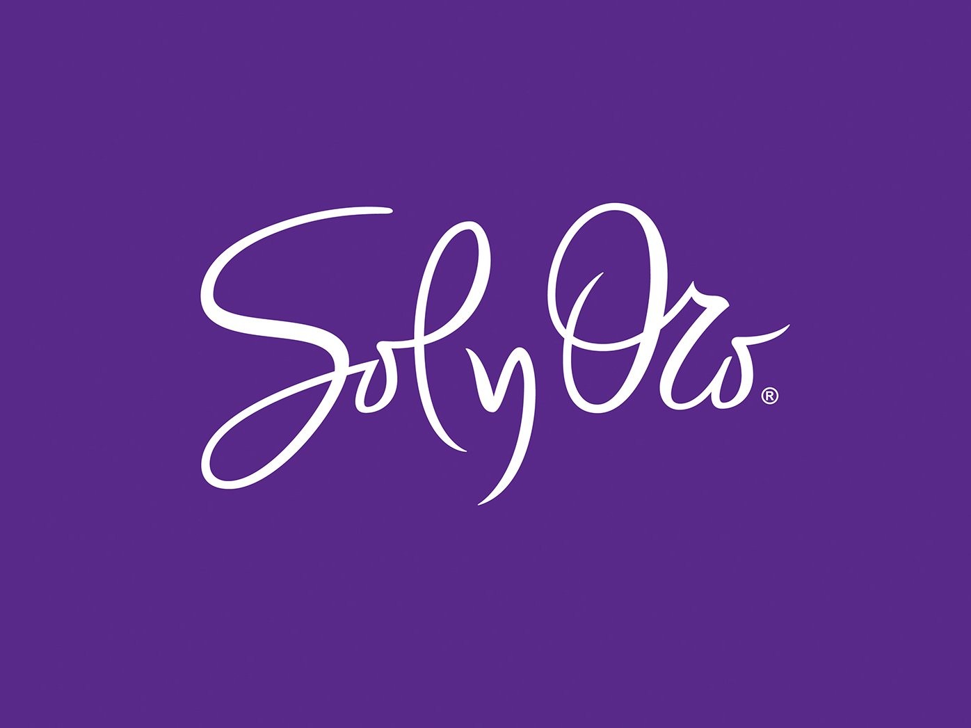 Etiqueta de ropa morada con la cursiva "Sofy Oro" y "TALLE 90" impresa en plata. El tejido de encaje es parcialmente visible, creando un tono elegante.