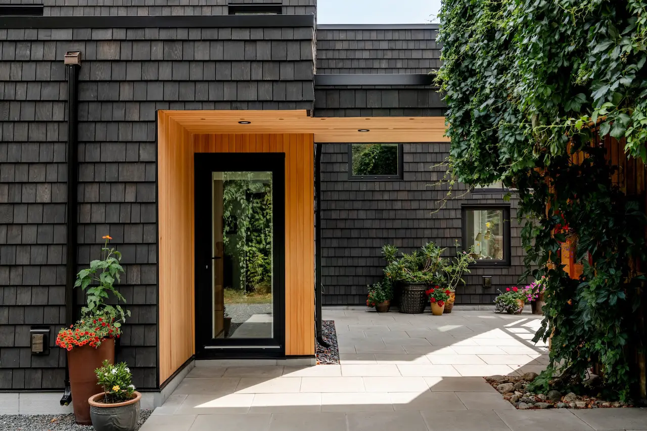 Modern two-story home with large glass windows, warmly lit interiors, and a balcony. Surrounded by trees and a manicured lawn at dusk. Cozy ambiance.